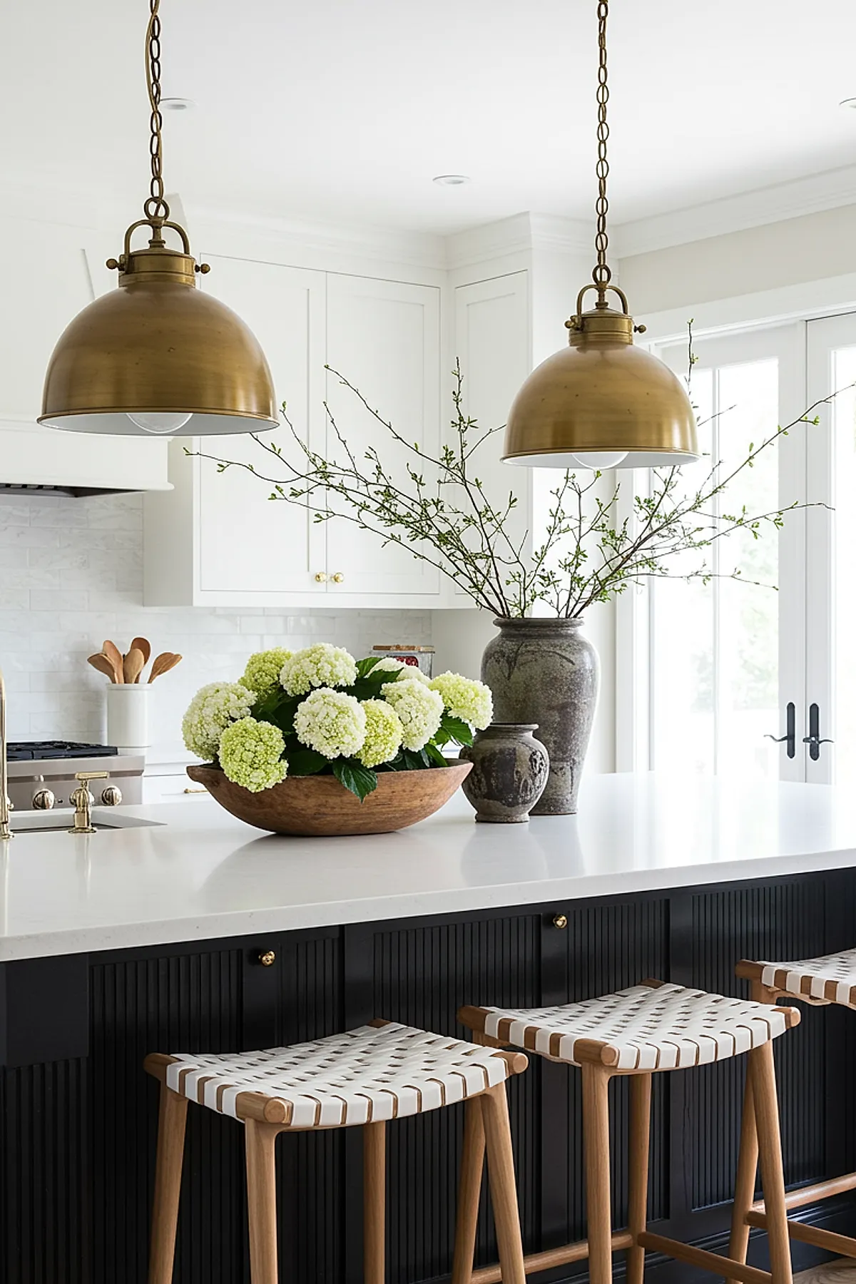 Brass dome pendant lights above a white kitchen island with wooden stools and floral decor.