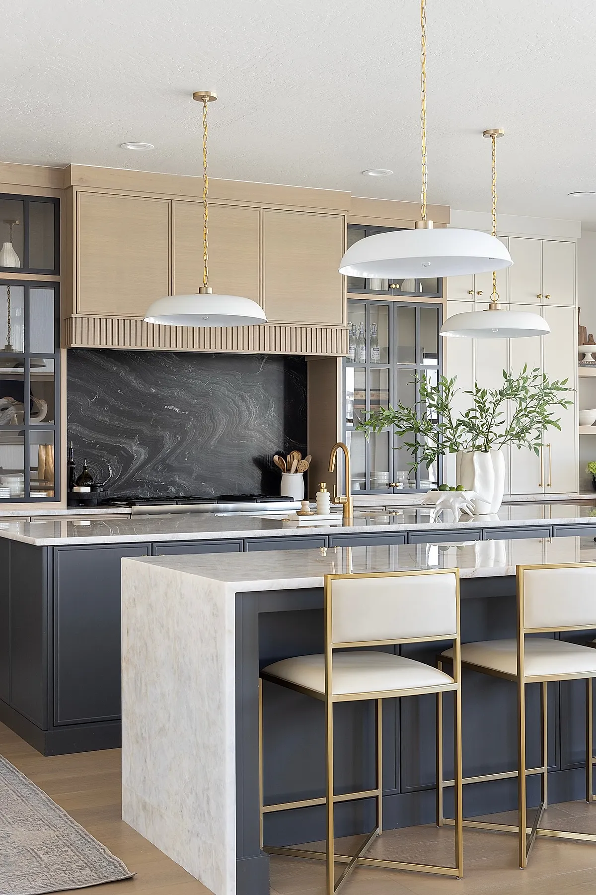 White dome pendant lights with gold chains hang above a marble kitchen island with bar stools.
