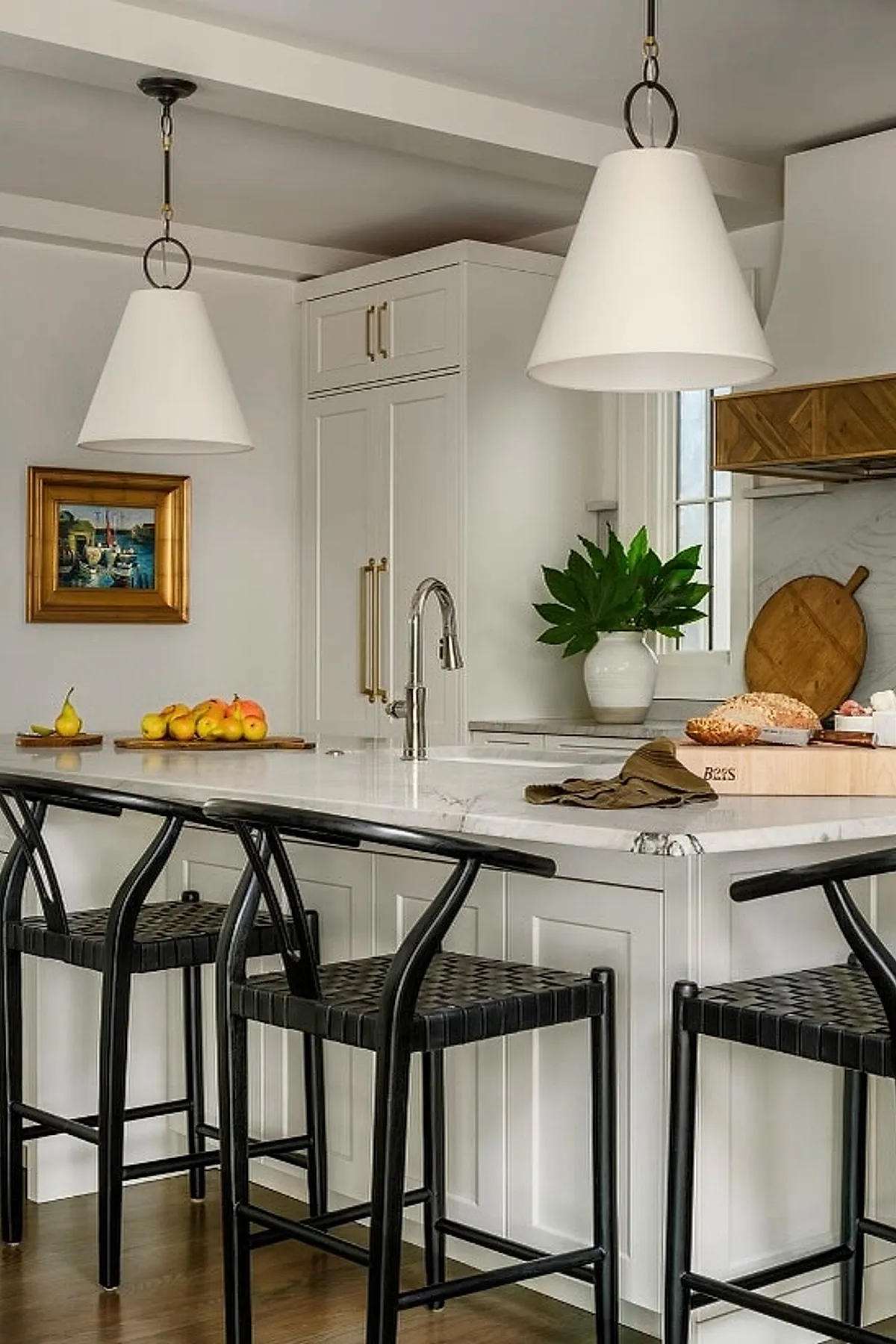 White cone pendant lights over a marble kitchen island with black bar stools.