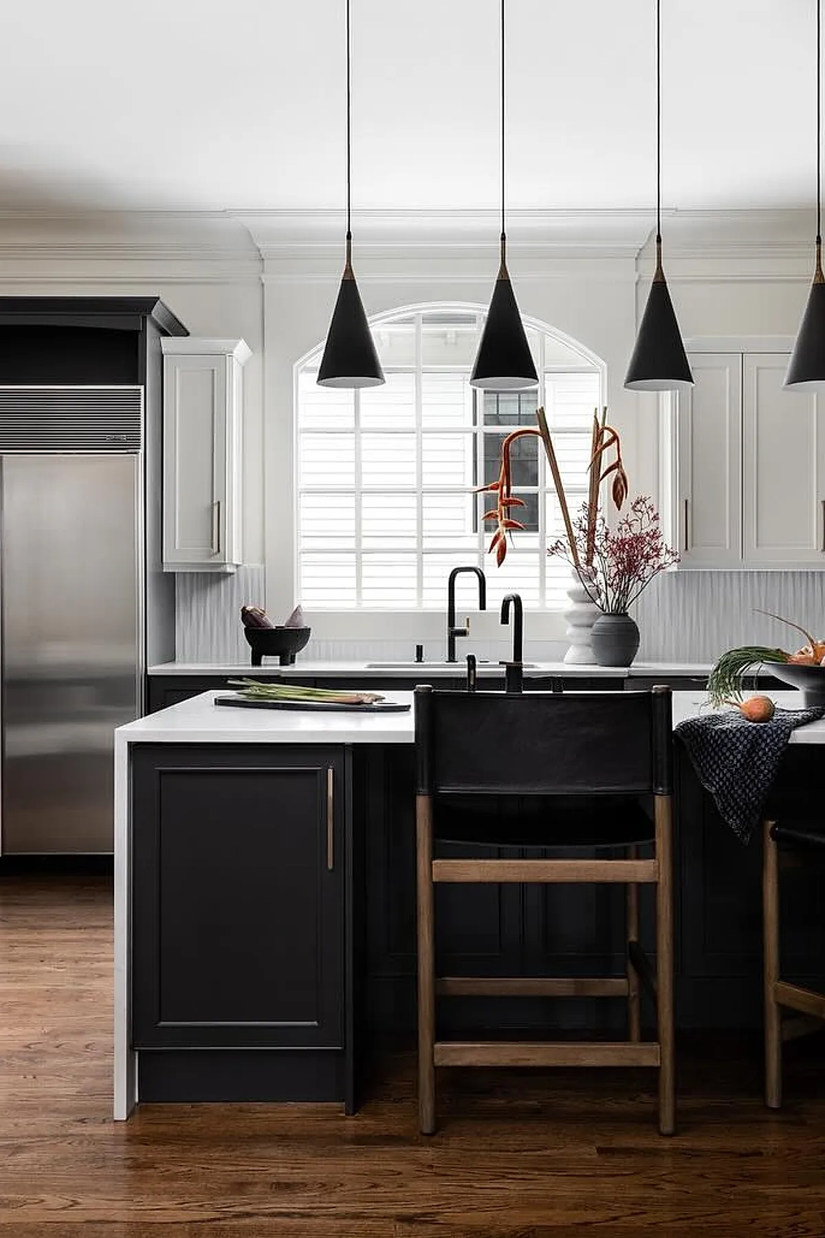 Black cone pendant lights hang over a white kitchen island with black and wood bar stools.