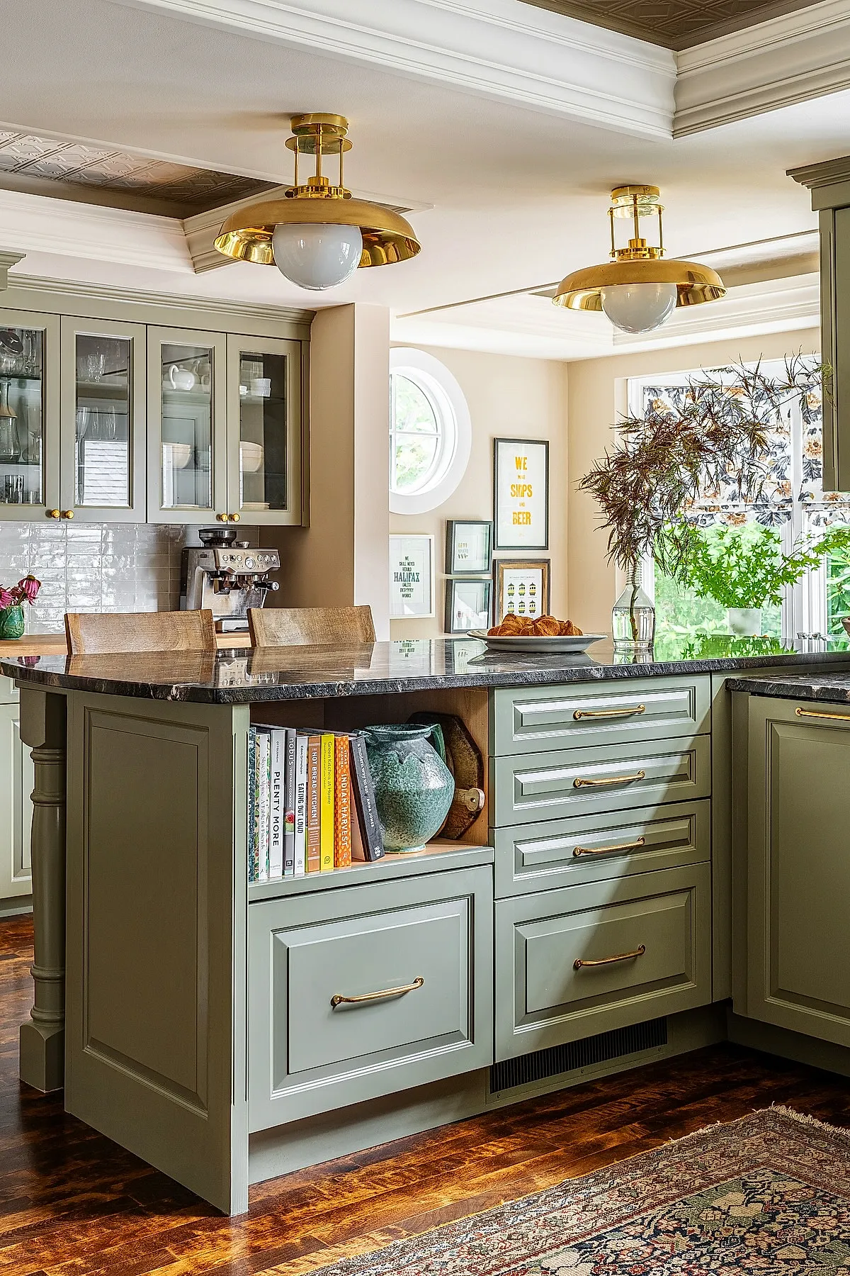Brass ceiling lights over green cabinetry kitchen island with books and decor.