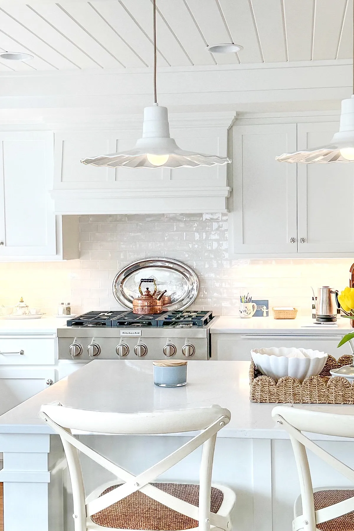 White wavy-edged pendant lights hang over a kitchen island with white cabinetry.