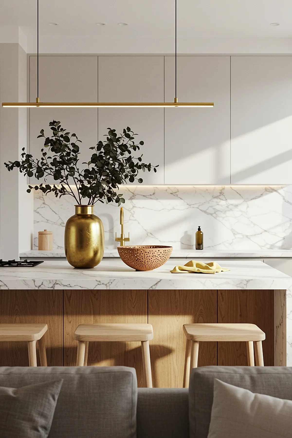 Slim brass bar light above a marble kitchen island with wooden stools and golden vase.