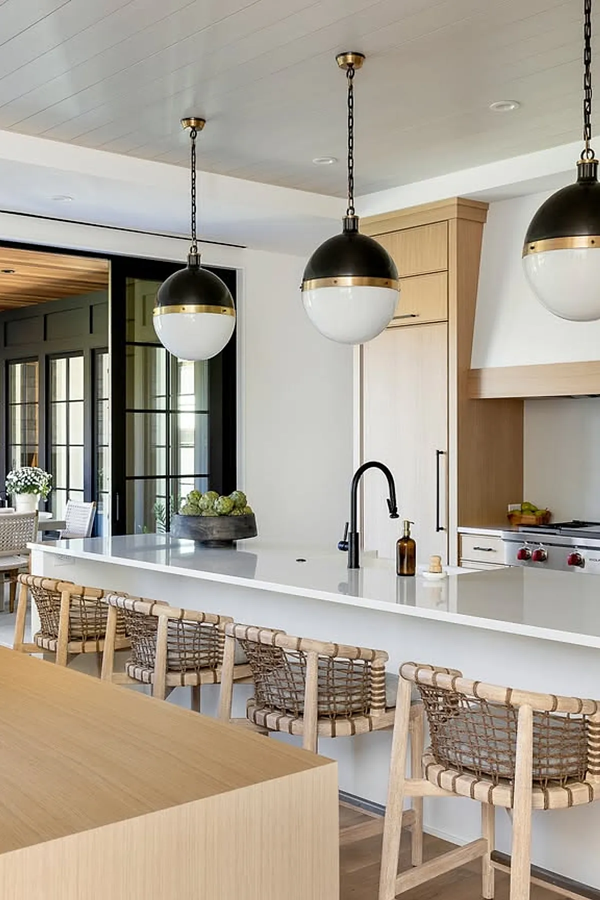 Black and white globe pendant lights with brass accents above a kitchen island with woven chairs.