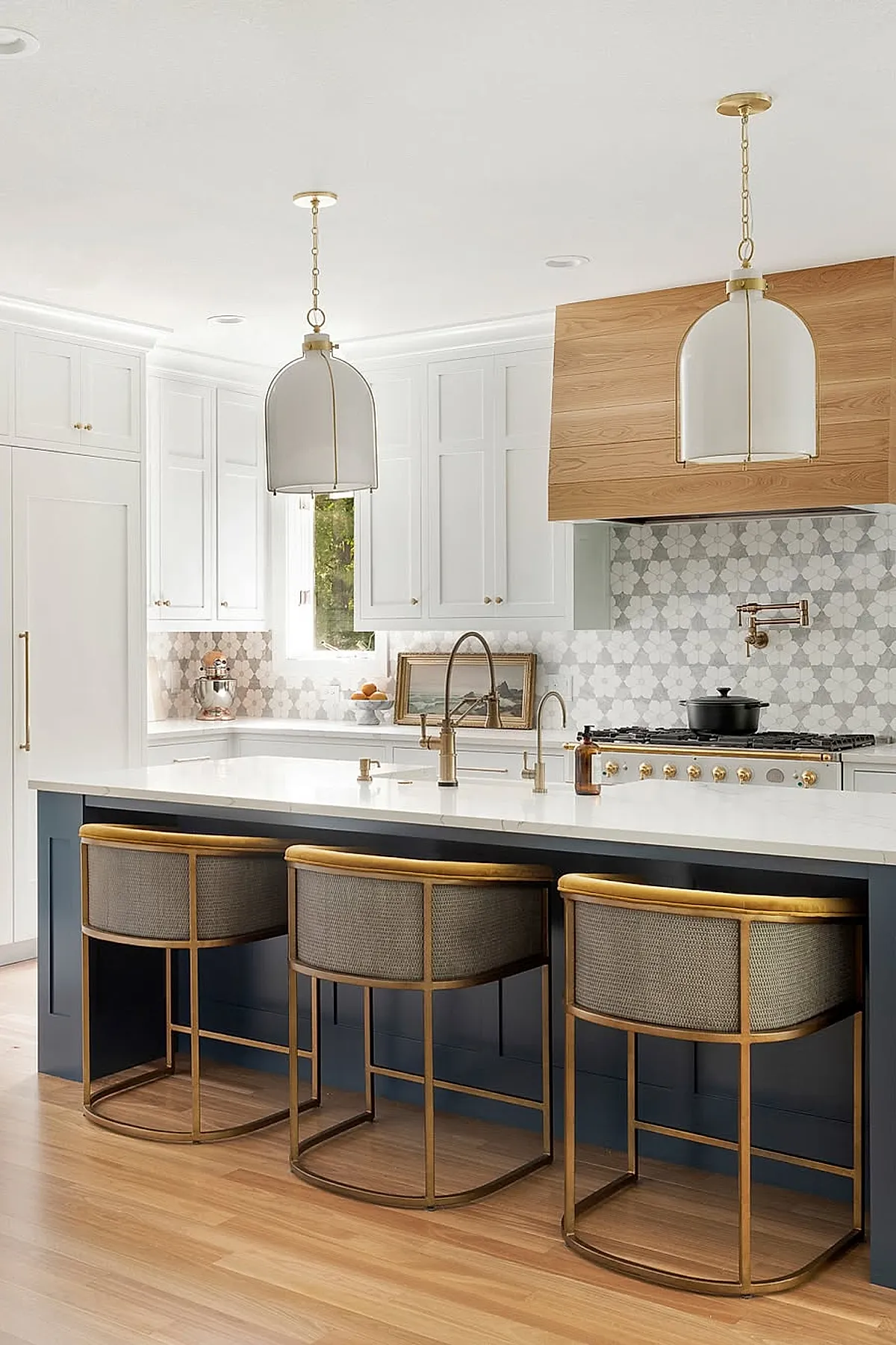 Frosted glass pendant lights with brass accents over a kitchen island and cushioned stools.