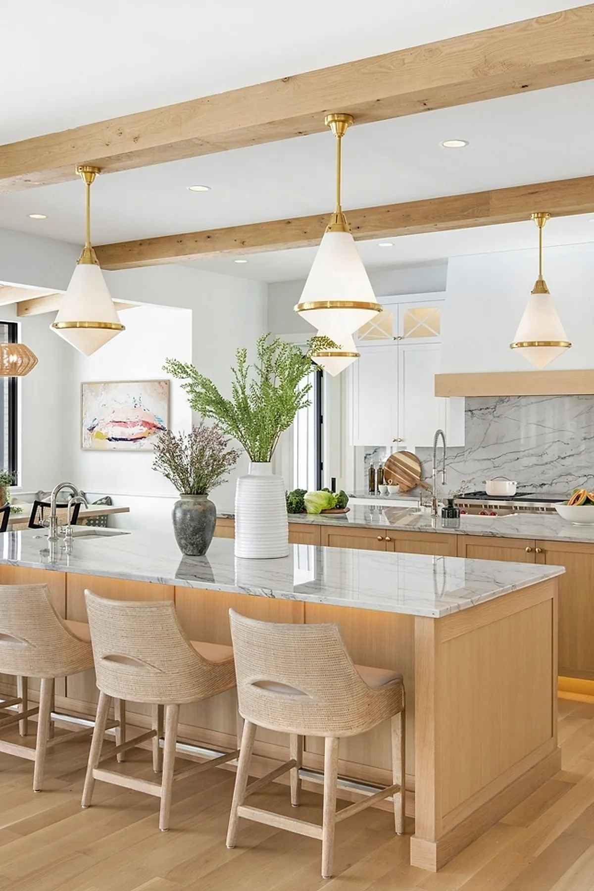 Cone pendant lights with brass accents above a kitchen island with marble countertop and wooden beams.