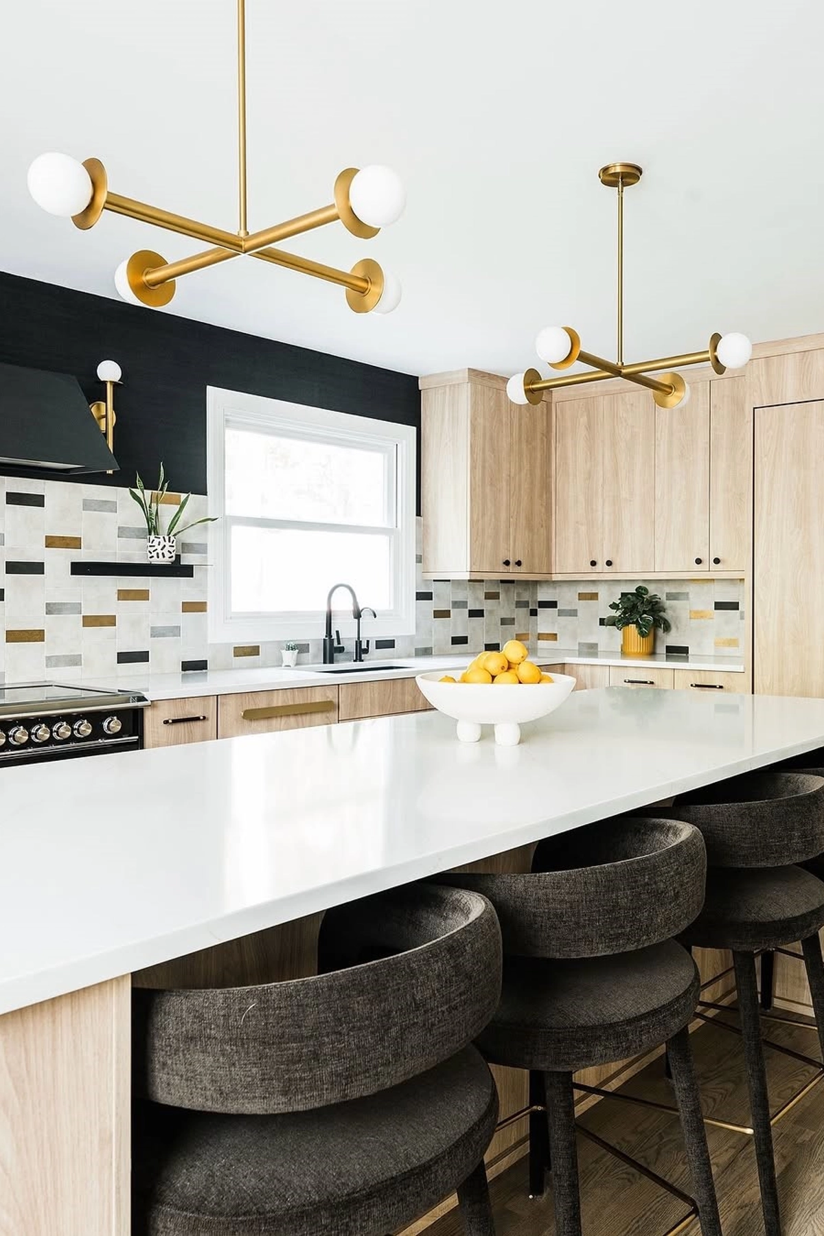 Brass globe pendant lights over a white kitchen island with black bar stools and wood cabinetry.