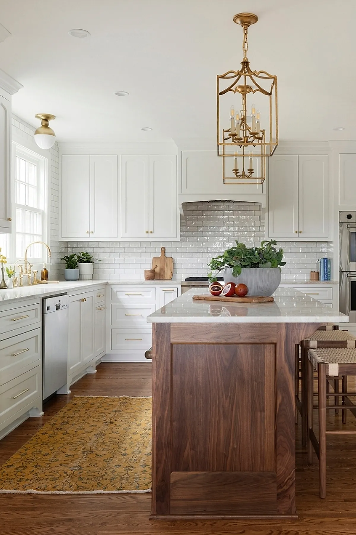 Brass chandelier above kitchen island with white cabinets, wood accents, and a rug.