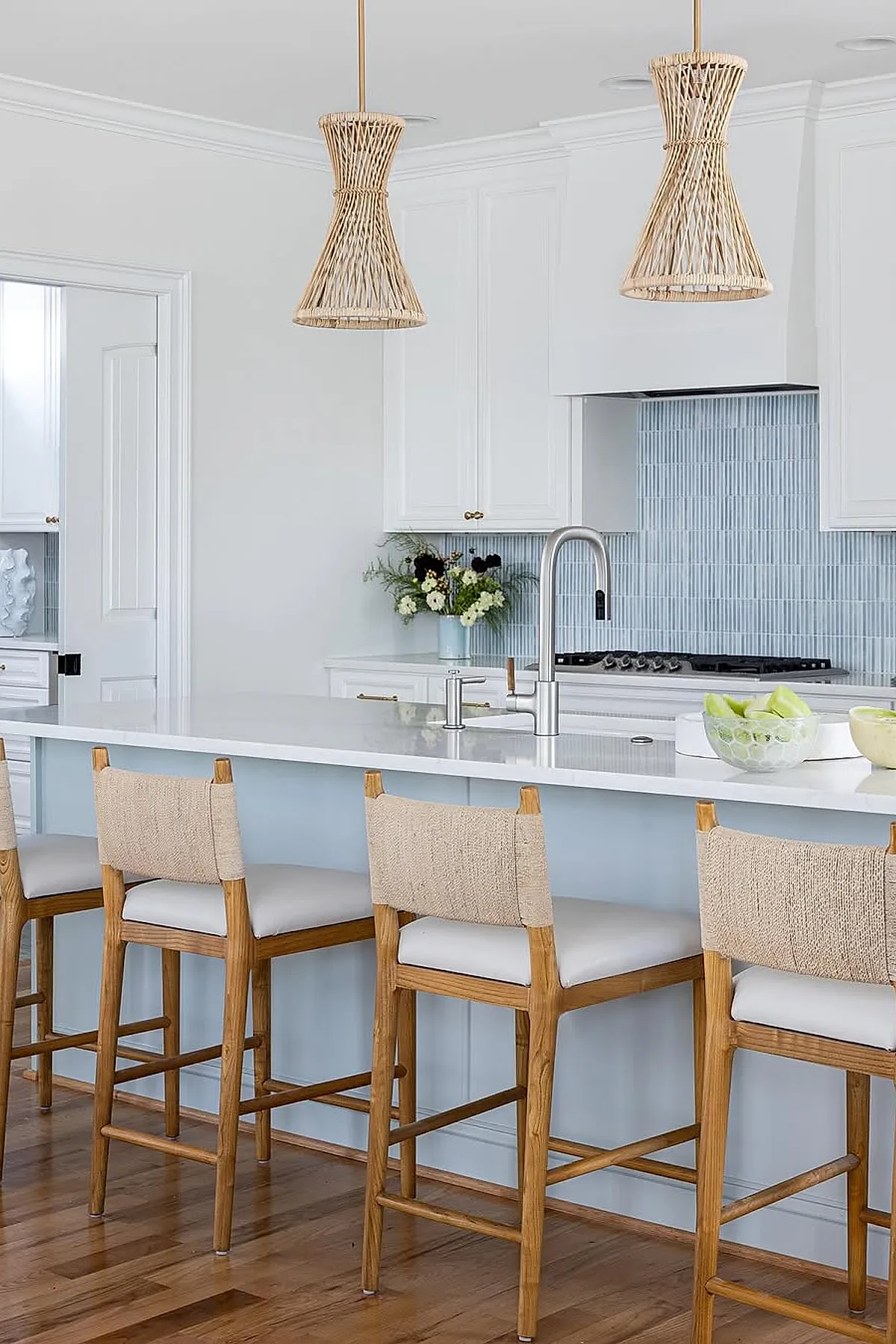 Woven rattan pendant lights hang over a white kitchen island with wooden bar stools and blue backsplash.
