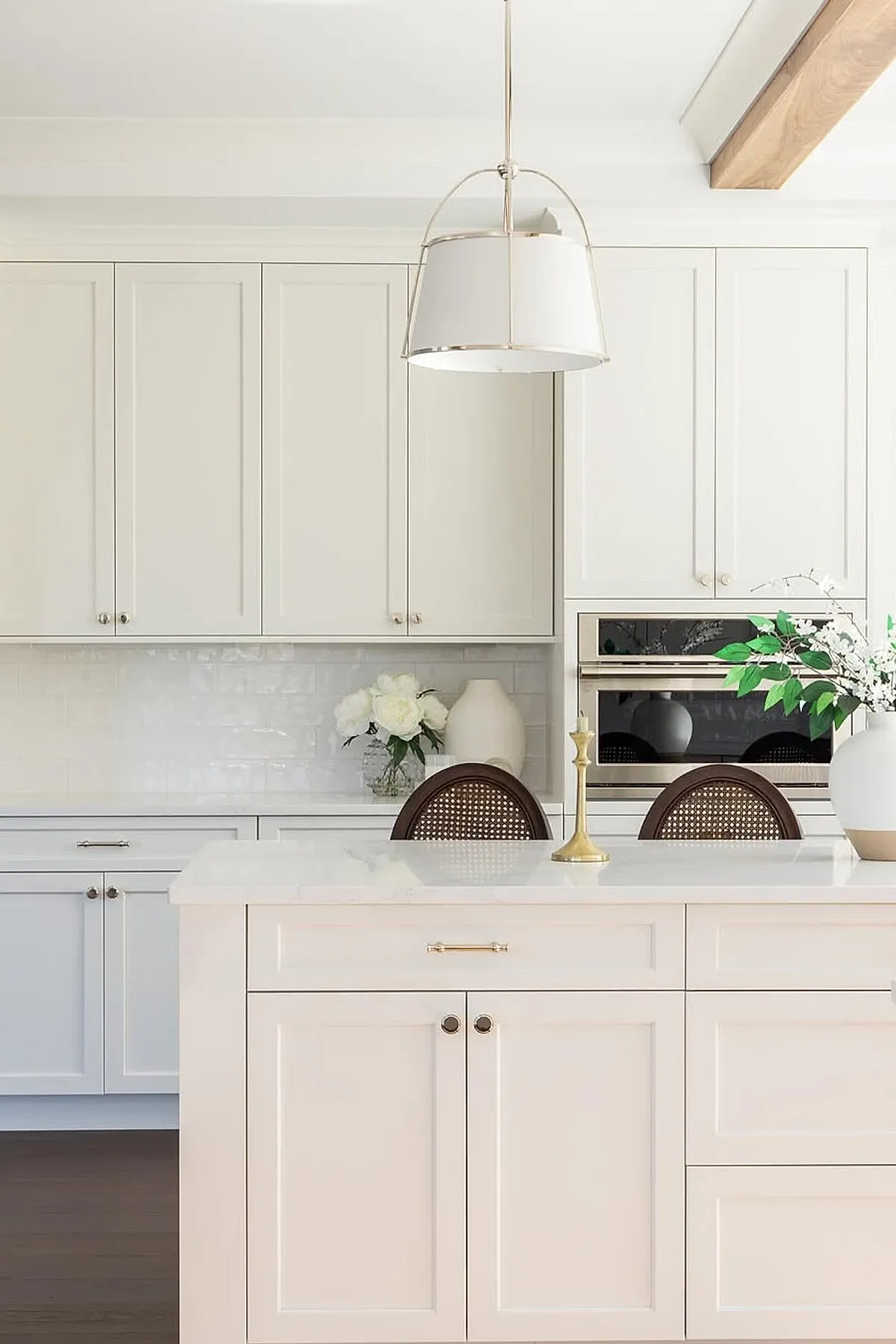 White drum pendant light above a kitchen island with white cabinets and brass hardware.