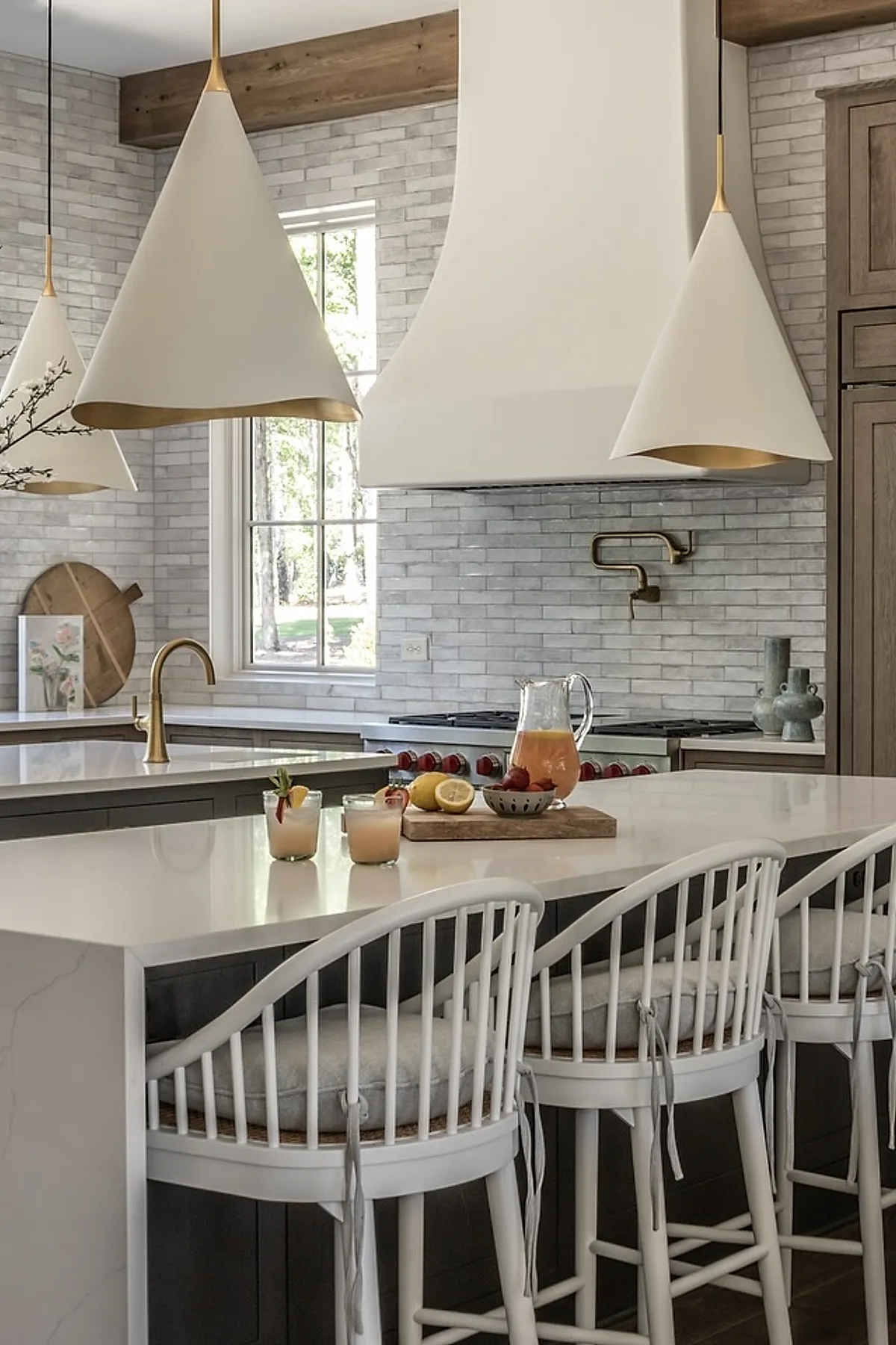 White cone pendant lights with gold interiors over a marble kitchen island with white chairs.