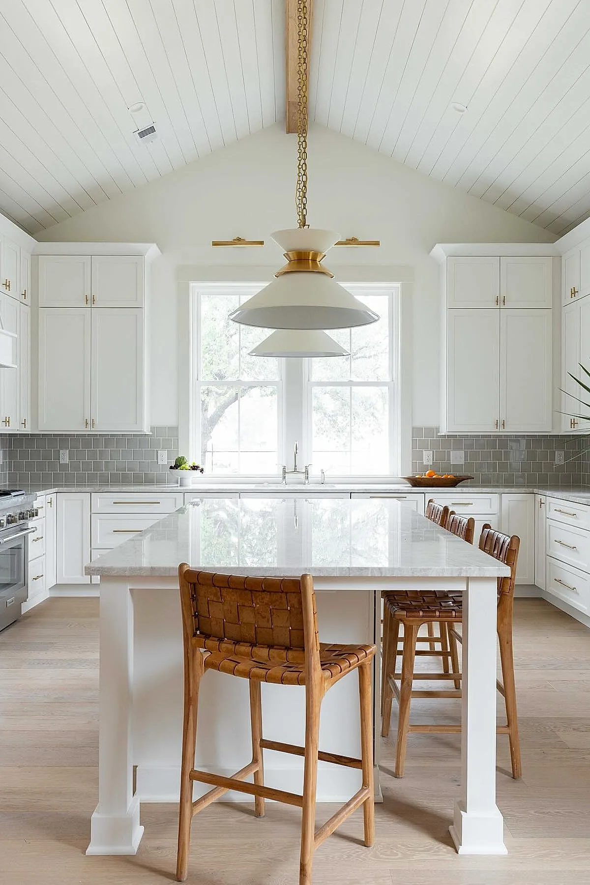 White pendant light with brass accents above kitchen island with woven chairs.