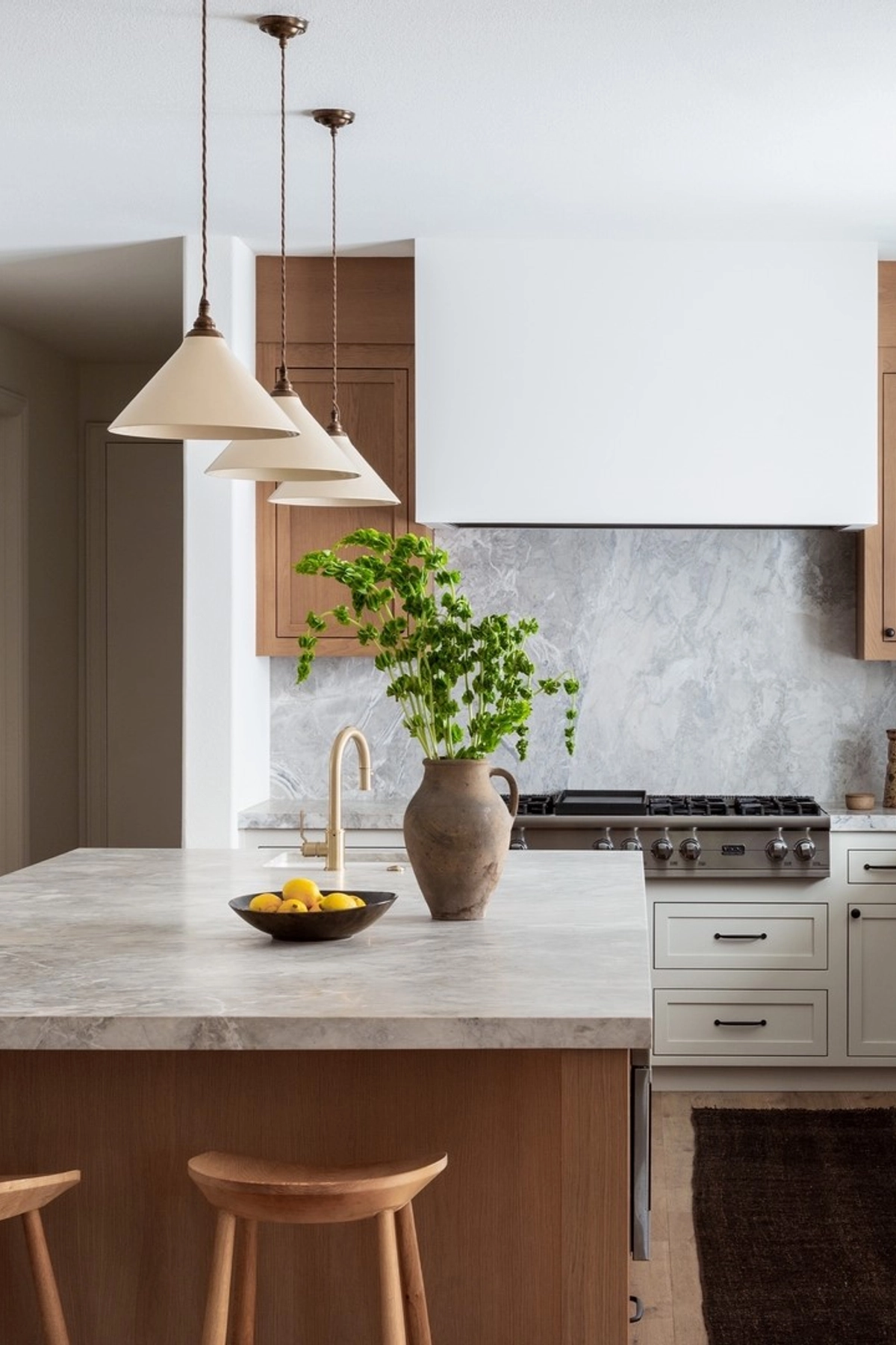 White cone pendant lights with brass details above a marble kitchen island with wooden cabinets.