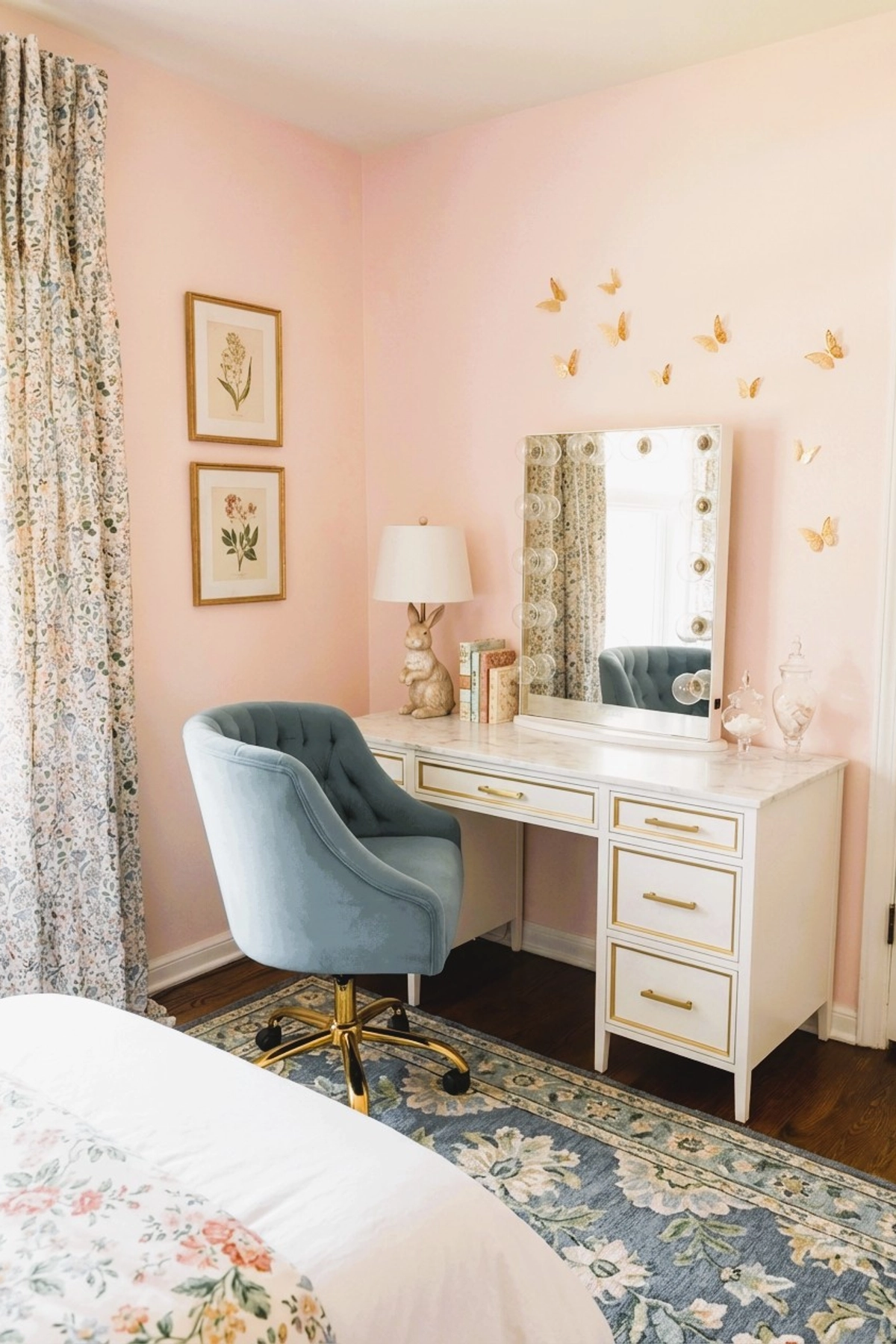 Preteen girl's bedroom vanity with a white and gold desk, velvet blue swivel chair, pink walls, gold butterfly wall accents, floral curtains, framed botanical prints, a bunny lamp, and a marble-style tabletop with books and decor.