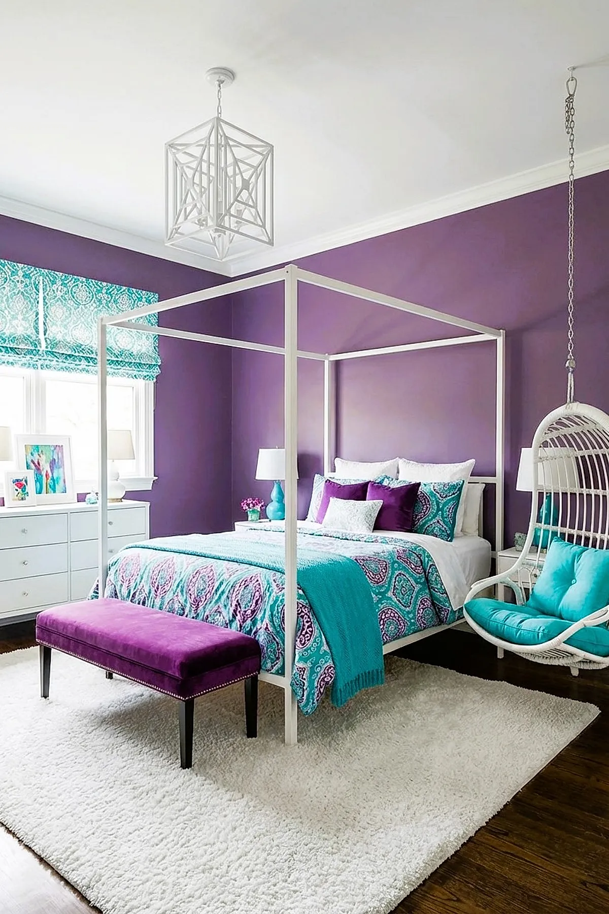 Girl's bedroom featuring deep purple walls with a white metal canopy bed dressed in teal and purple patterned bedding, accented by a purple velvet bench at the foot of the bed, white dresser under window with teal patterned roman shades, and a white hanging wicker chair with bright teal cushions on a fluffy white rug over dark hardwood flooring.