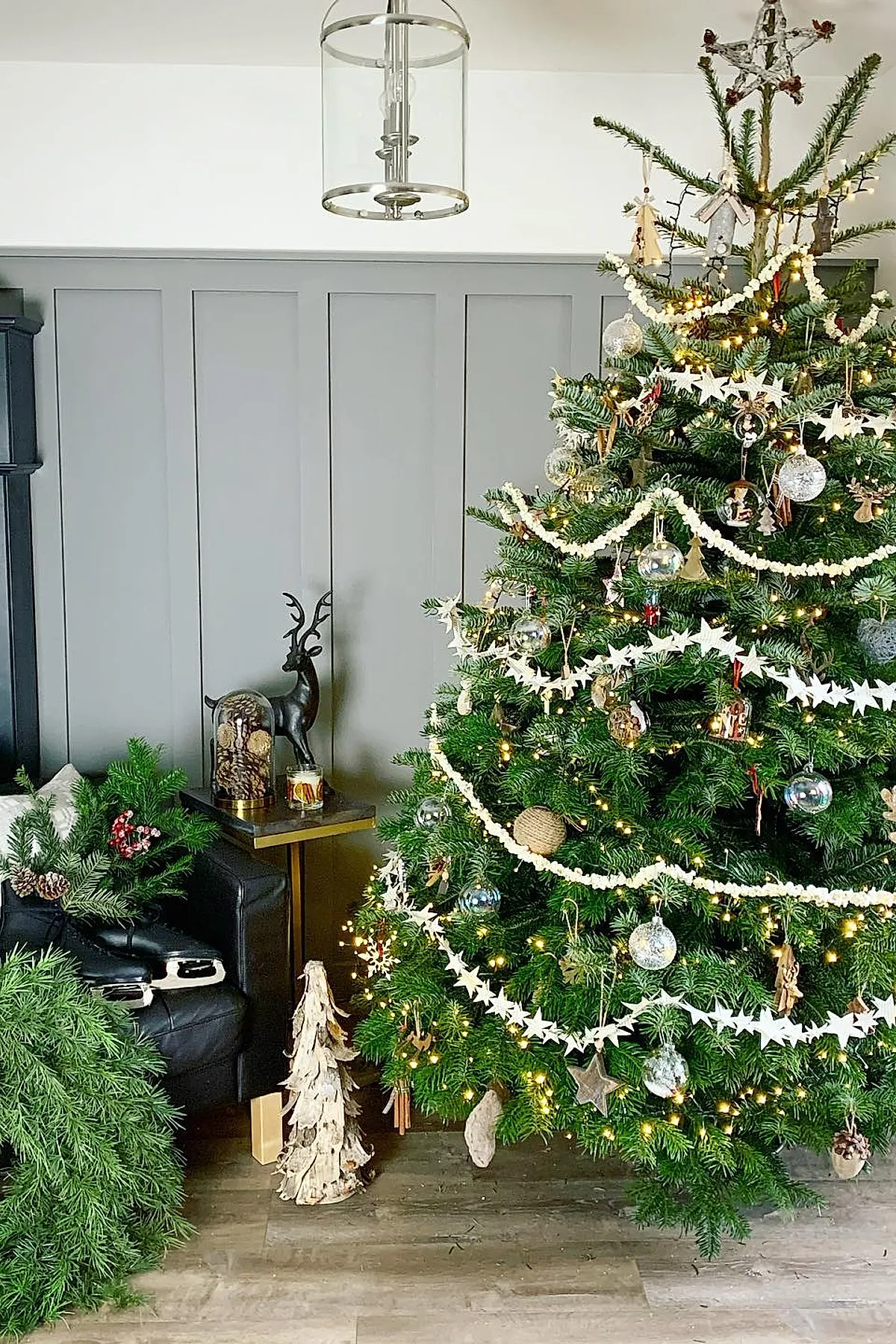 A traditional christmas tree decorated with white popcorn garlands, white star garlands, silver reflective baubles, rustic wooden ornaments, and warm white string lights topped with a woven star.