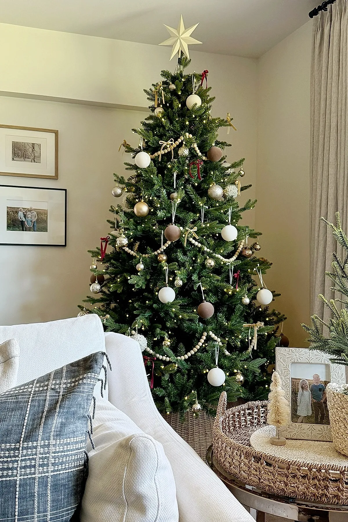 traditional christmas tree decorated with white, gold, and brown round ornaments, wooden bead garlands draped around the branches, small warm white lights, topped with a cream-colored star.