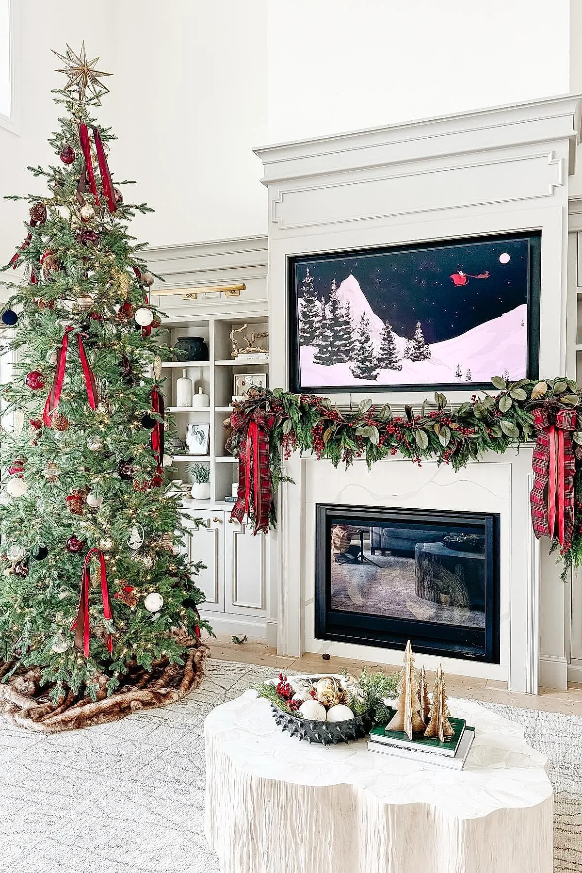 traditional christmas tree decorated with long red velvet ribbons, red and gold ornaments, topped with a gold star beside a fireplace mantle adorned with magnolia leaf and berry garland tied with large plaid bows.