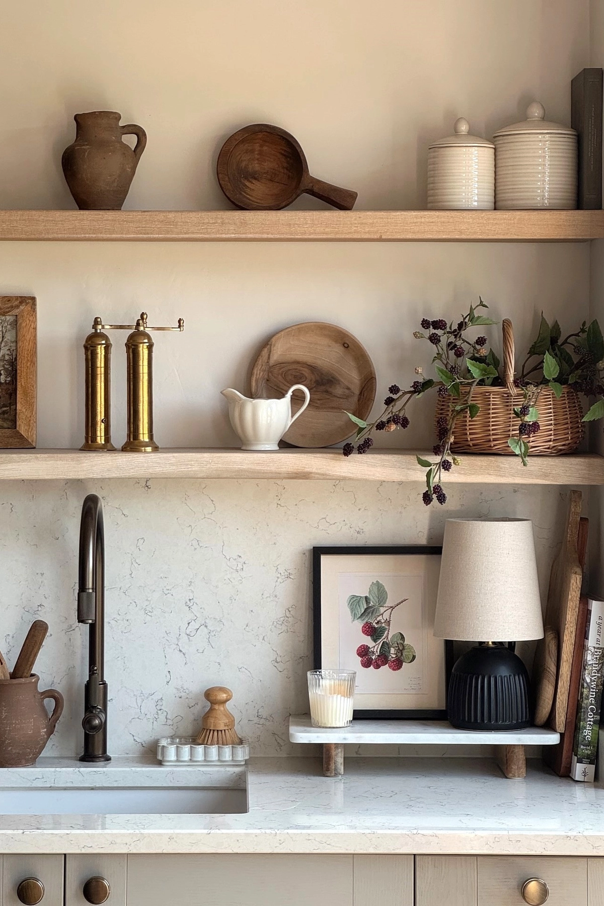 Kitchen with open shelves displaying rustic pottery, woven basket with berries, framed art, and books on a white marble countertop.
