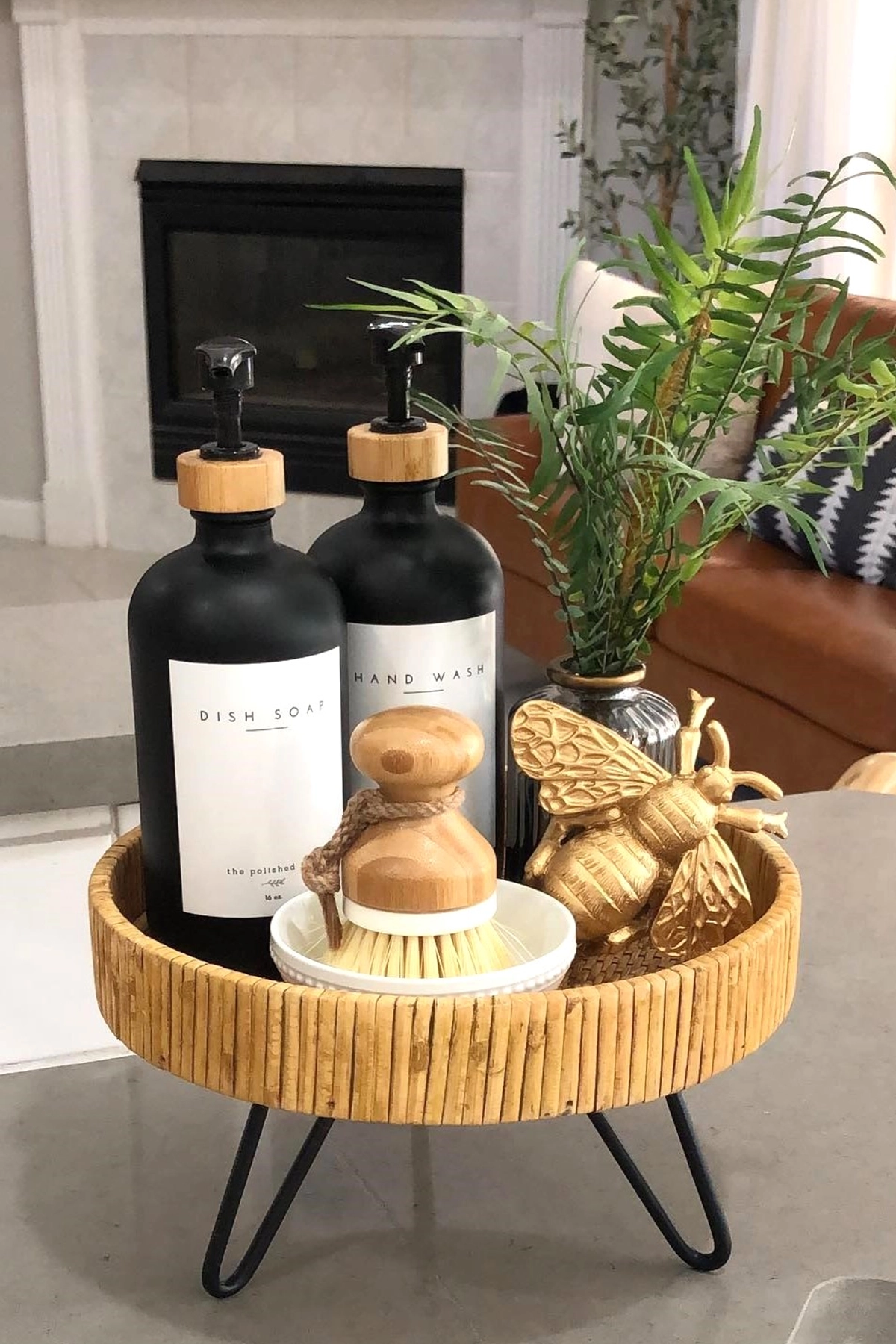 Bamboo tray on kitchen countertop with black soap dispensers, a scrub brush, and gold bee decor.
