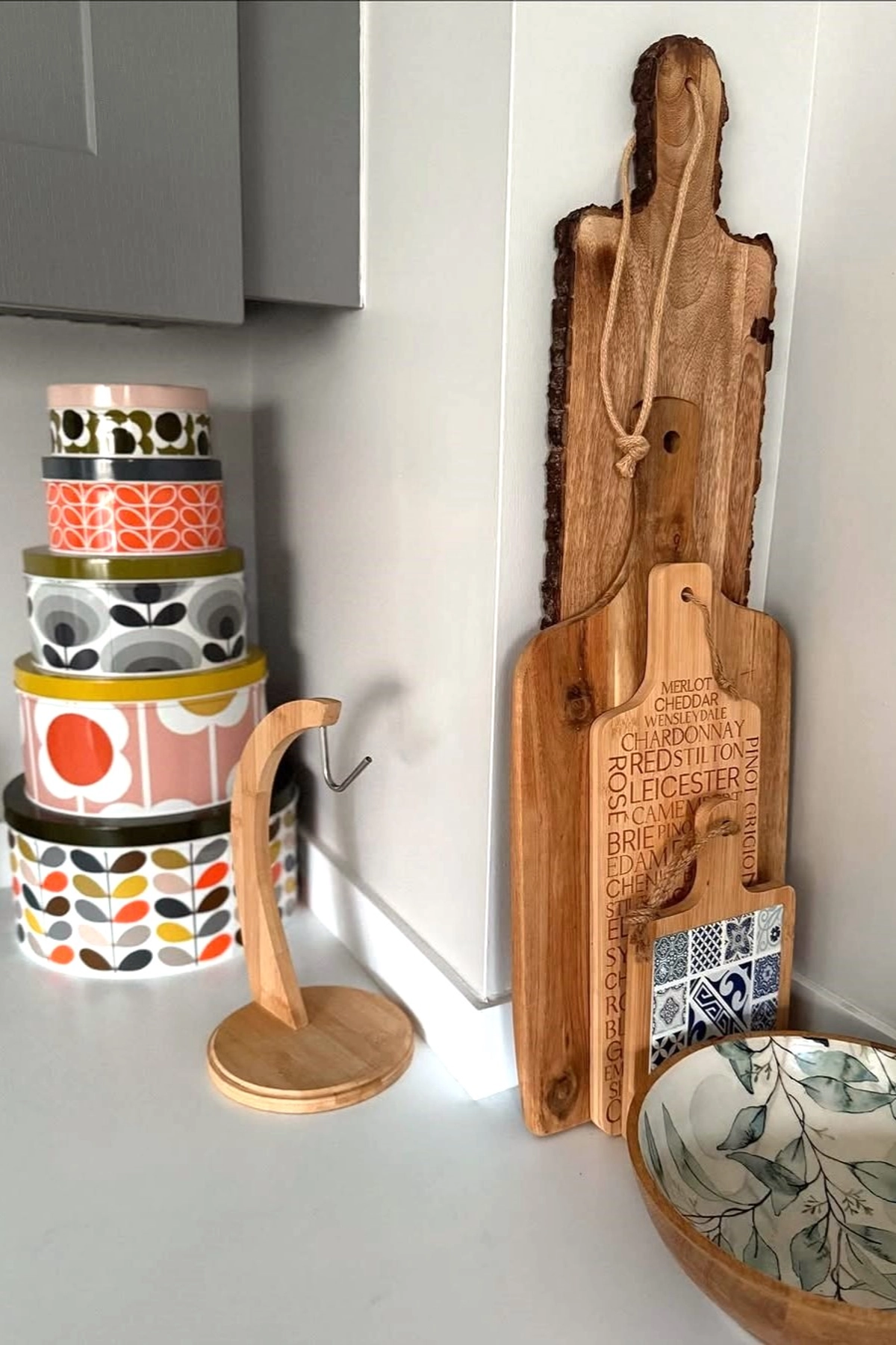 Kitchen countertop featuring vintage patterned tins, wooden cutting boards, paper towel holder, and decorative bowl.