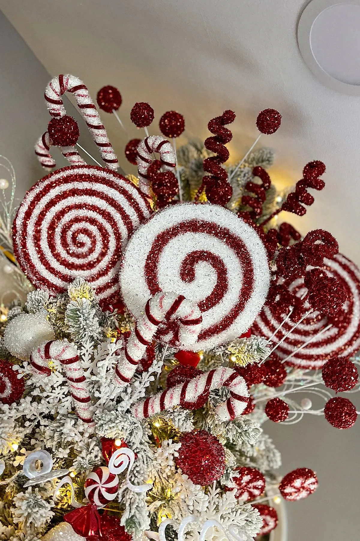 Close up of a candy cane christmas tree theme featuring glittery red and white peppermint spiral ornaments, candy cane shaped decorations, frosted pine branches, red glitter balls, and warm fairy lights.