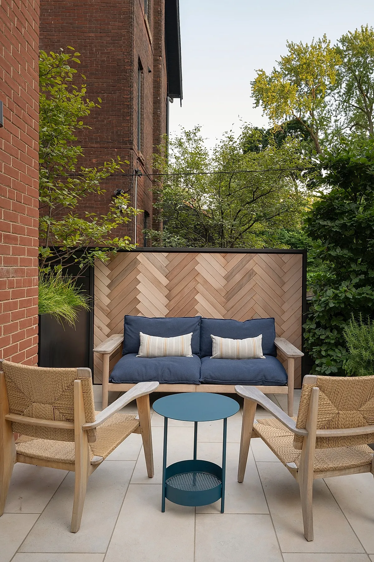 Patio with herringbone wood privacy screen, blue cushioned sofa, and woven chairs.