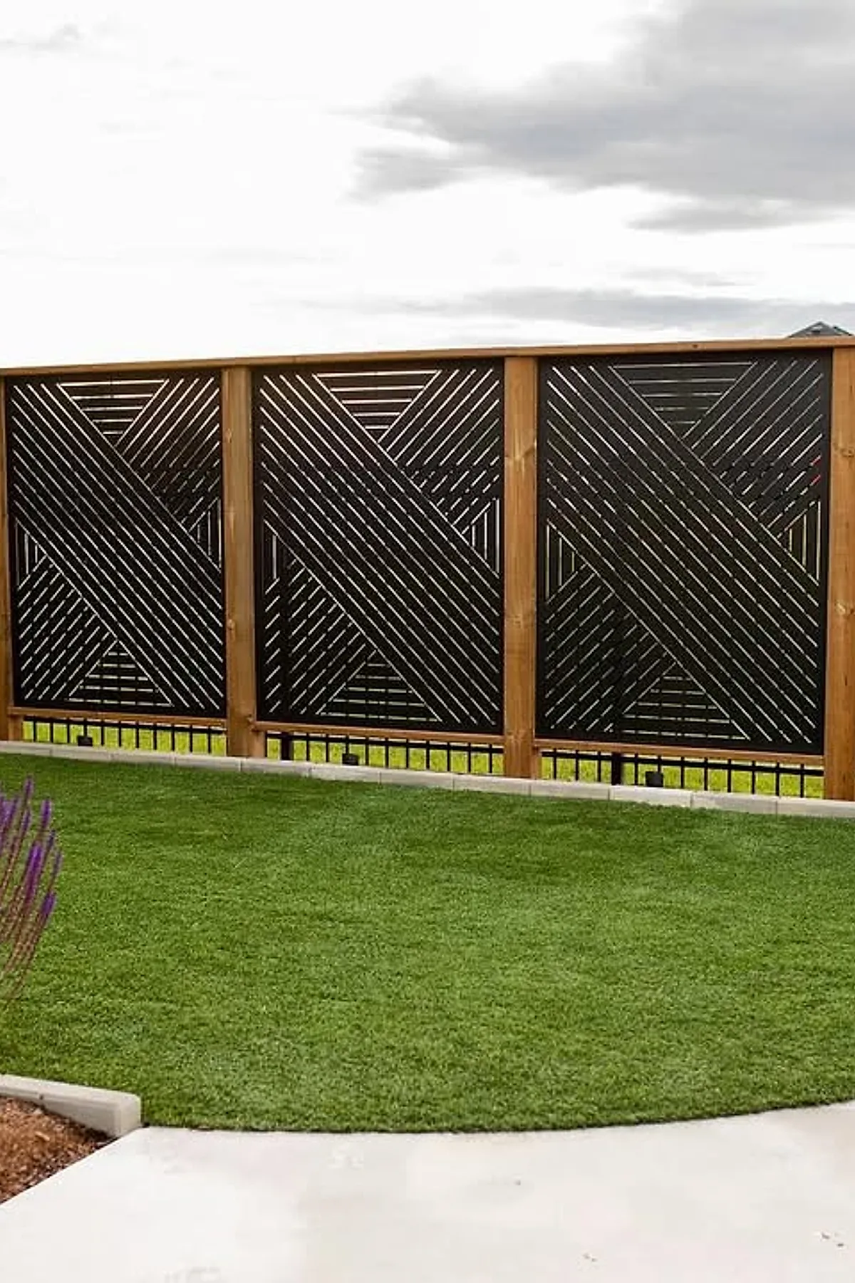 Wooden privacy screen with black geometric diagonal patterns and wooden frames in a backyard.