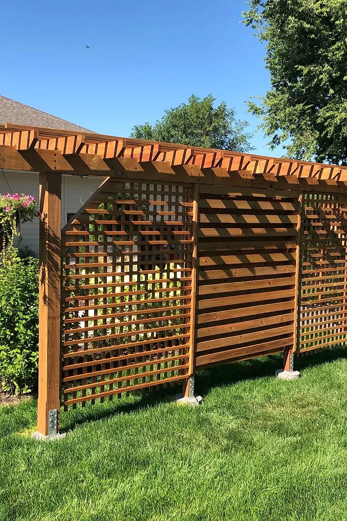 Wooden lattice privacy screen and arbor with mixed horizontal and vertical slats in a sunny backyard.