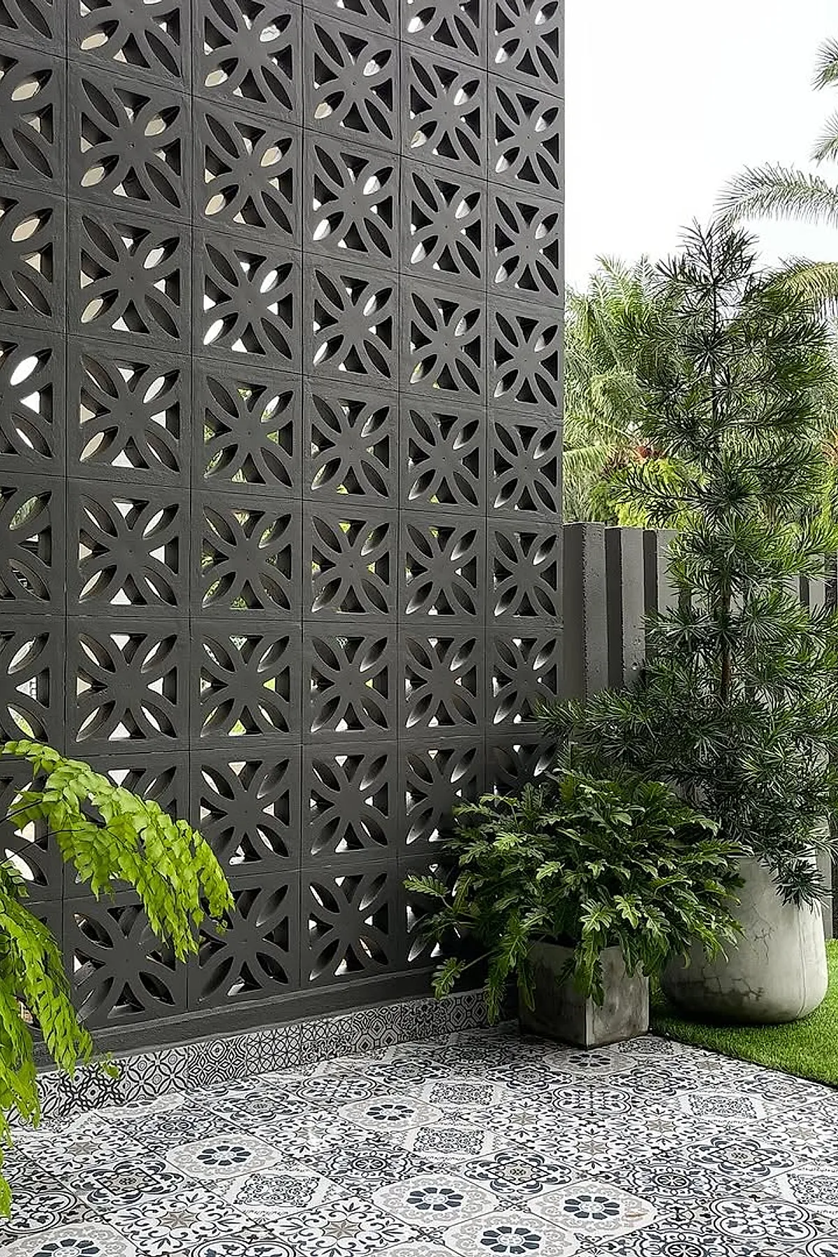 Decorative black breeze block wall with intricate patterns, surrounded by greenery and patterned tiles.