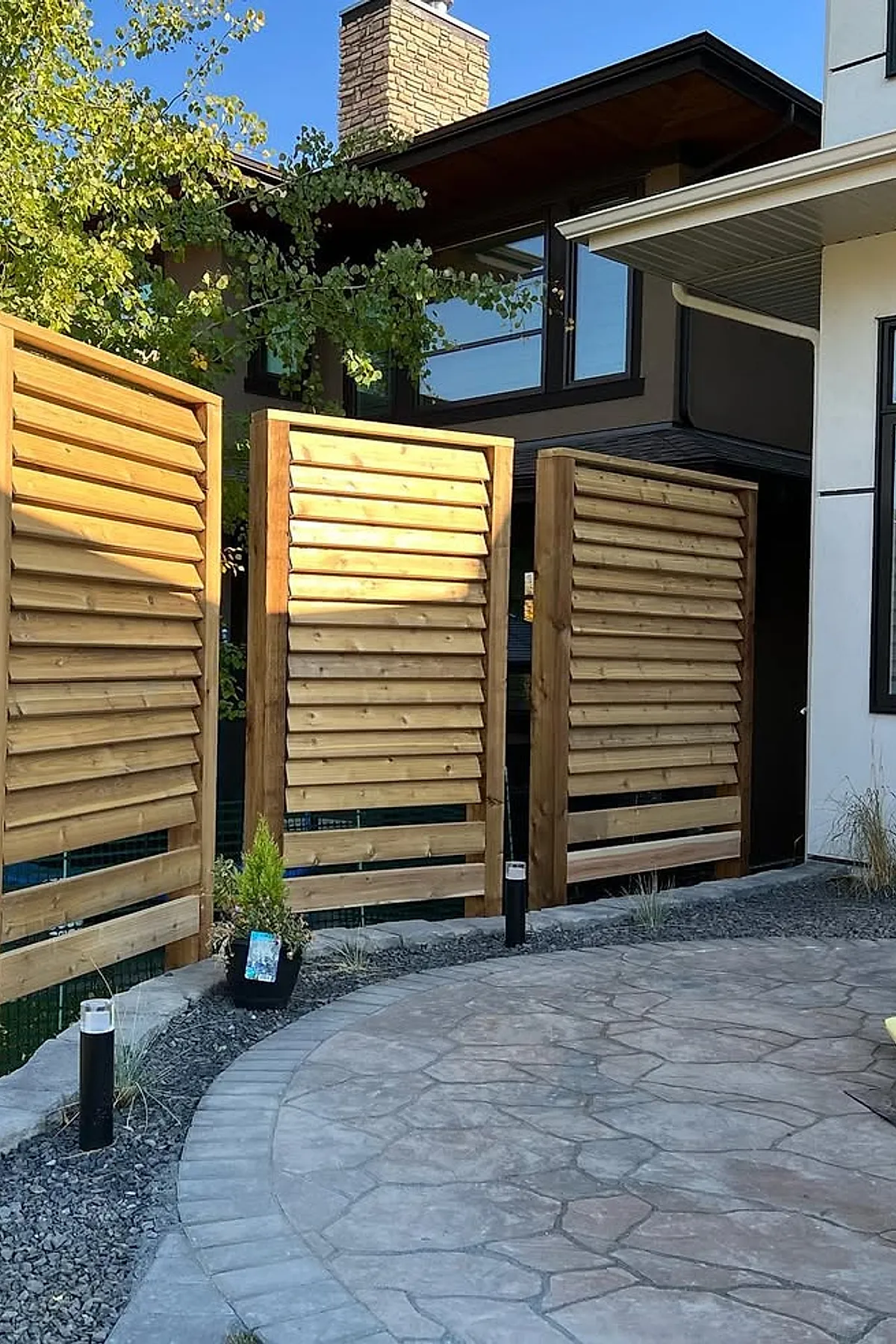 Wooden louvered privacy panels with a natural finish installed in a modern backyard setting.