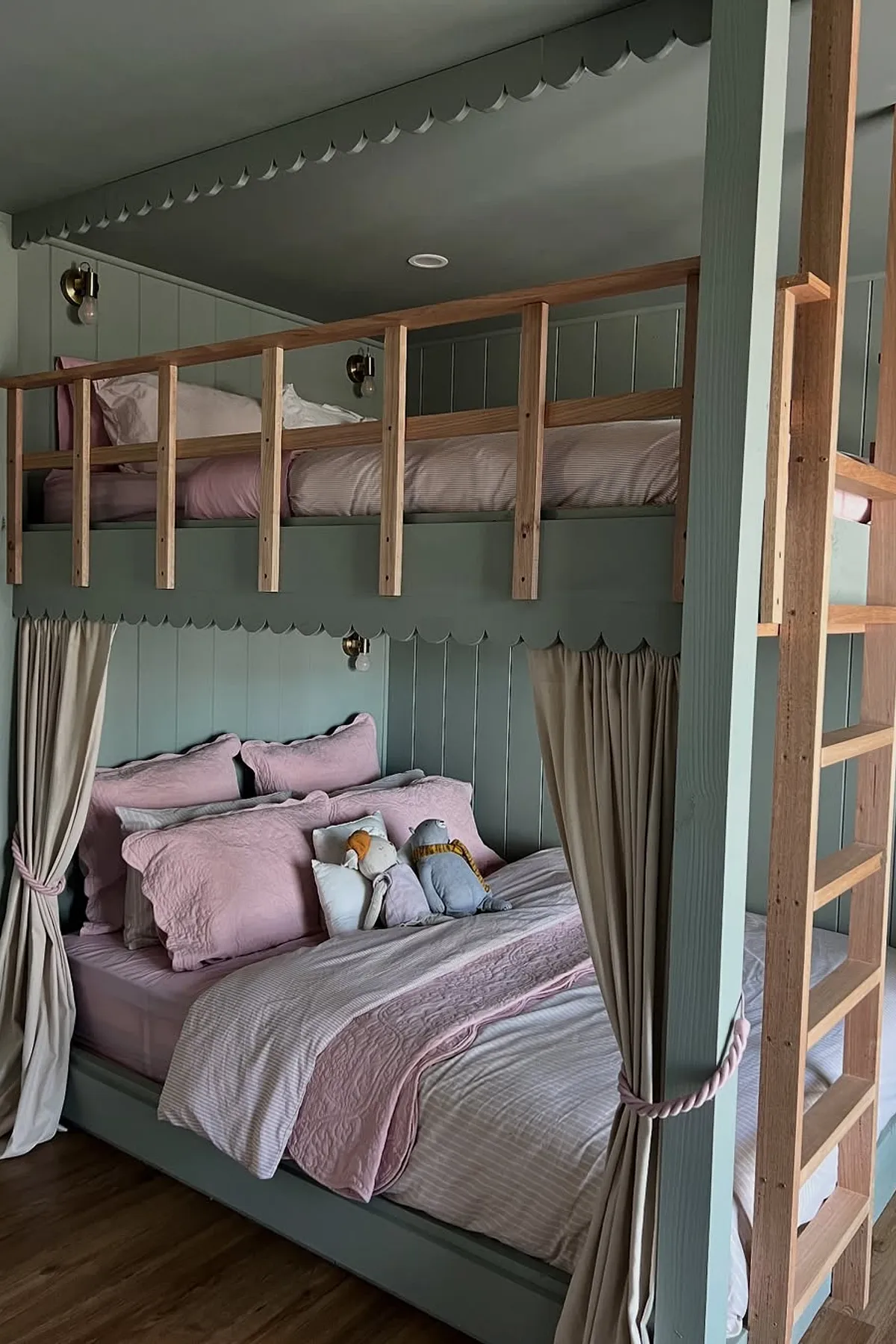 Bunk beds with scalloped trim, muted green color, and pink bedding.