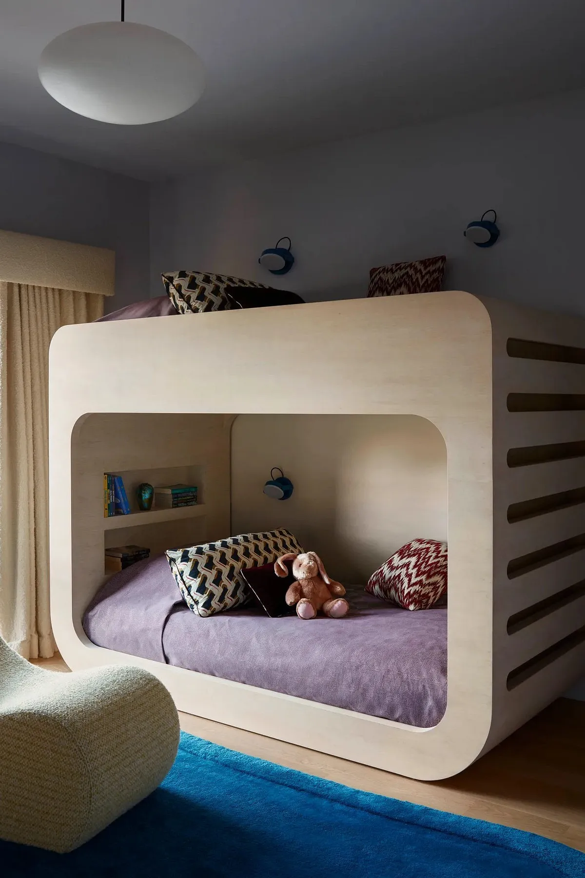 Modern built-in bunk beds with curved design, integrated shelves, patterned pillows, and a soft plush toy for added comfort.