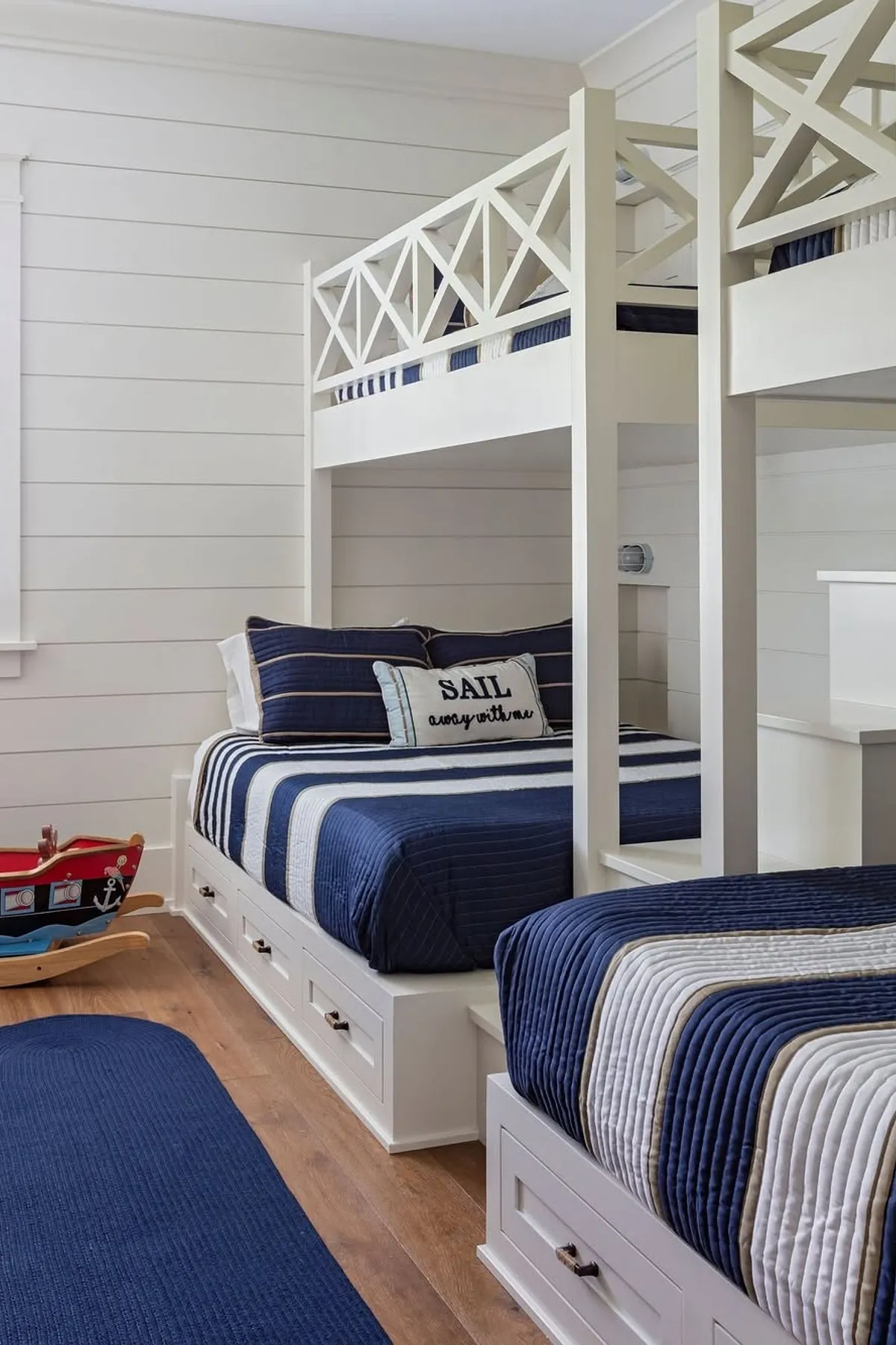 Nautical-themed built-in bunk beds with blue and white bedding, sailor motifs, and under-bed storage drawers.
