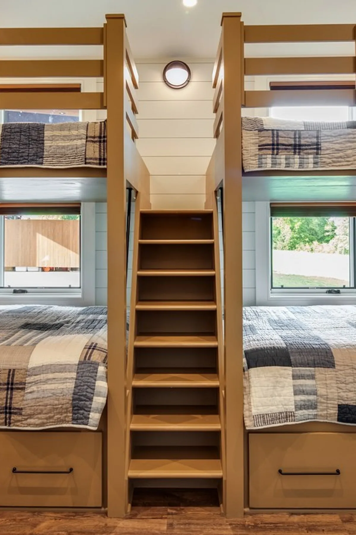 Built-in bunk beds with central staircase, storage drawers, quilted bedding, and large windows for natural light.