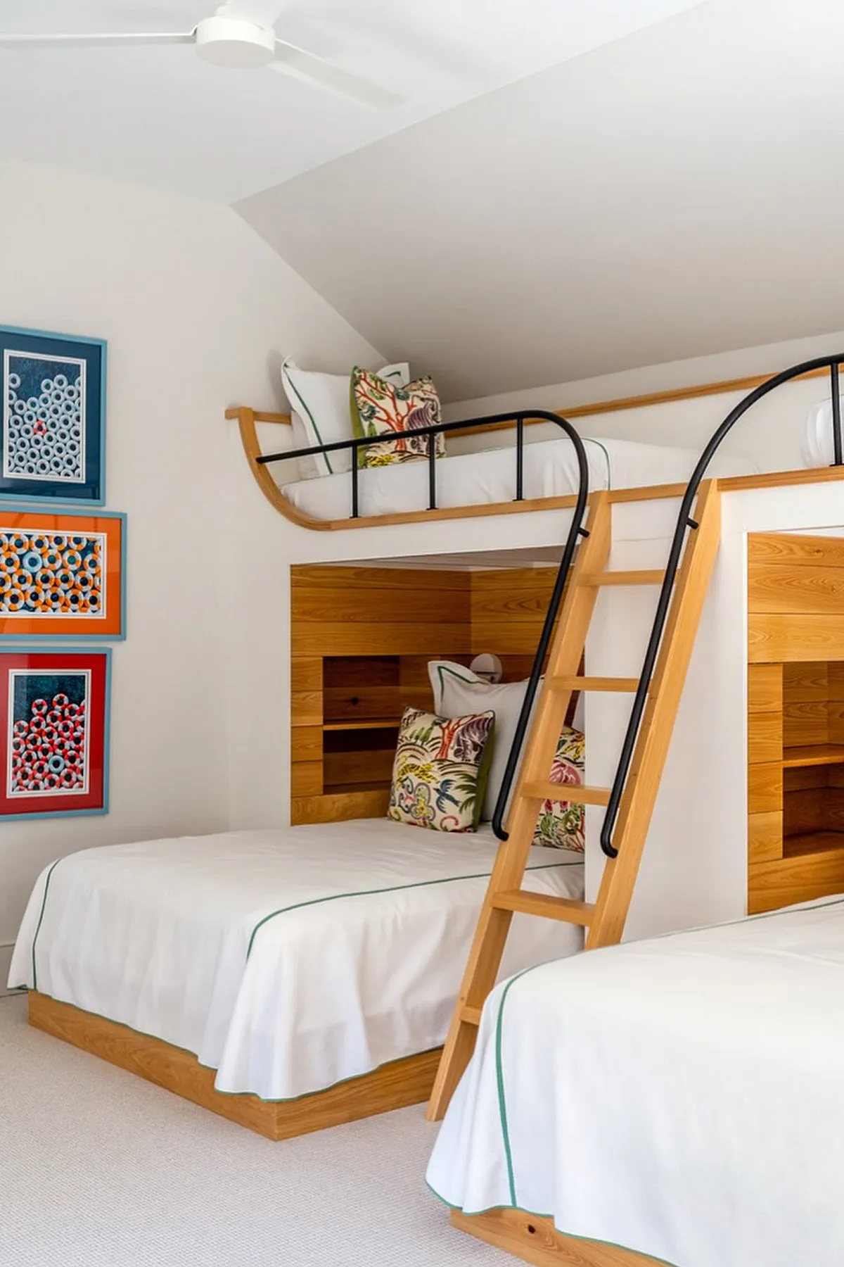 Built-in bunk beds with wooden frames, black railings, colorful artwork on walls, and integrated shelves for extra storage.