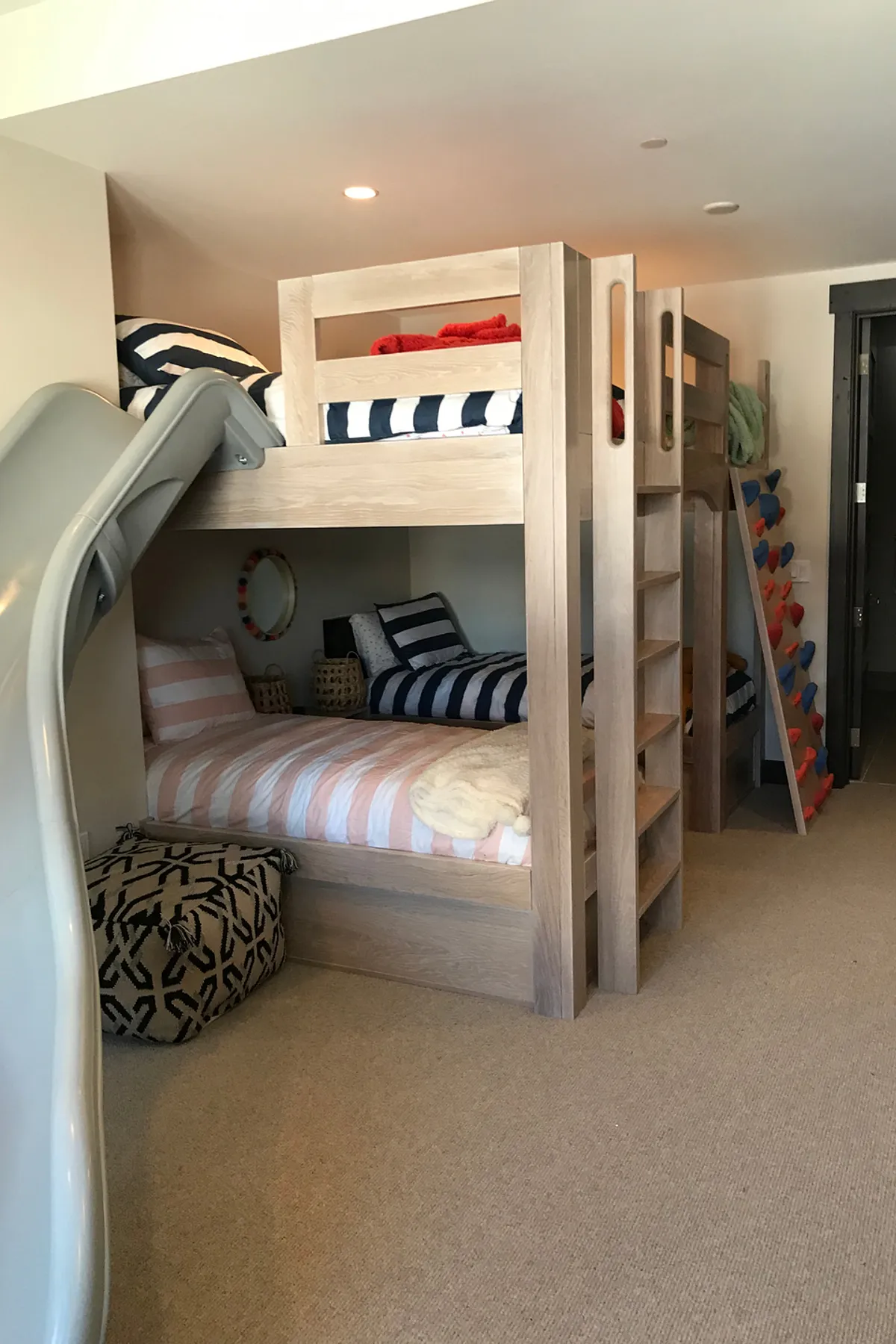 Built-in bunk beds with a slide, climbing wall, wooden ladder, and bold striped bedding in a playful children's room.