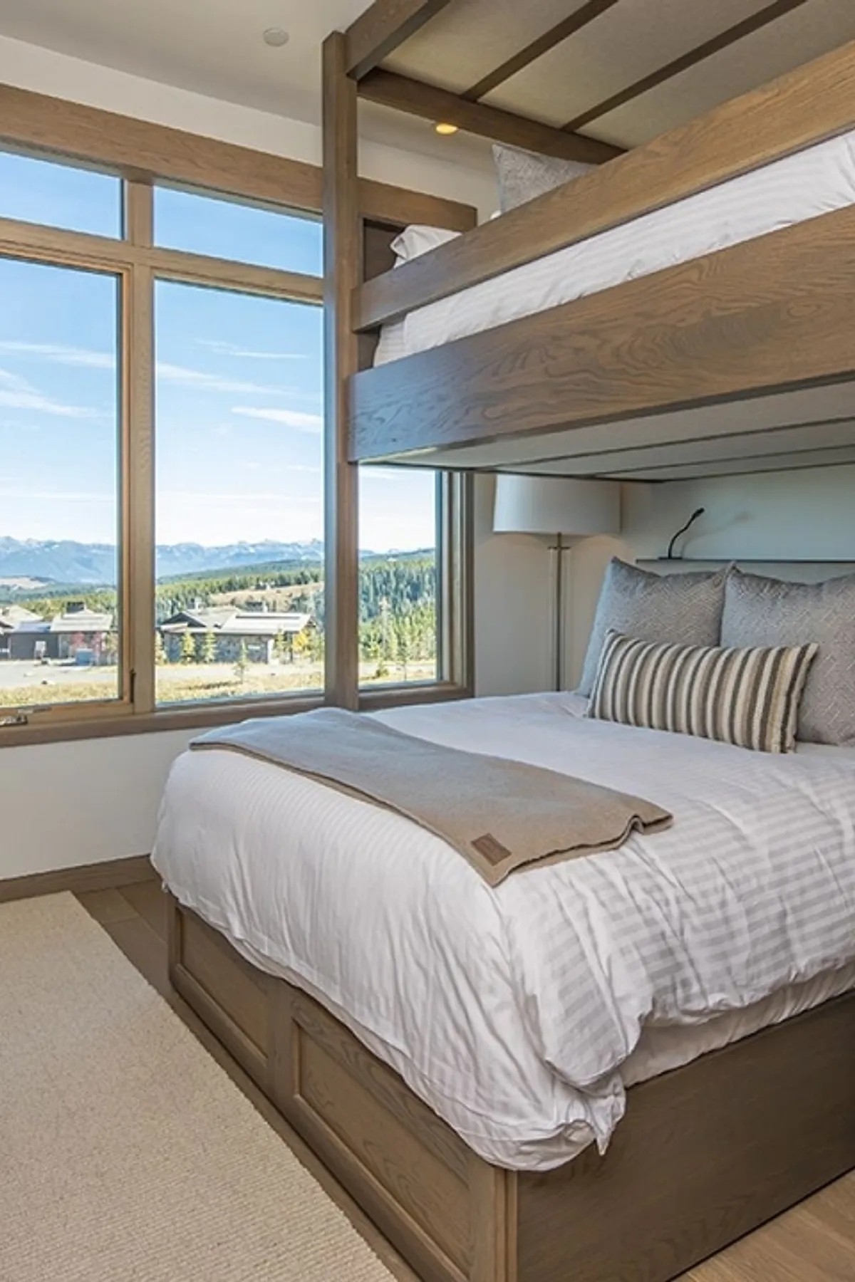 Built-in bunk beds with wood frame, neutral bedding, large windows offering scenic views, and a plush rug.