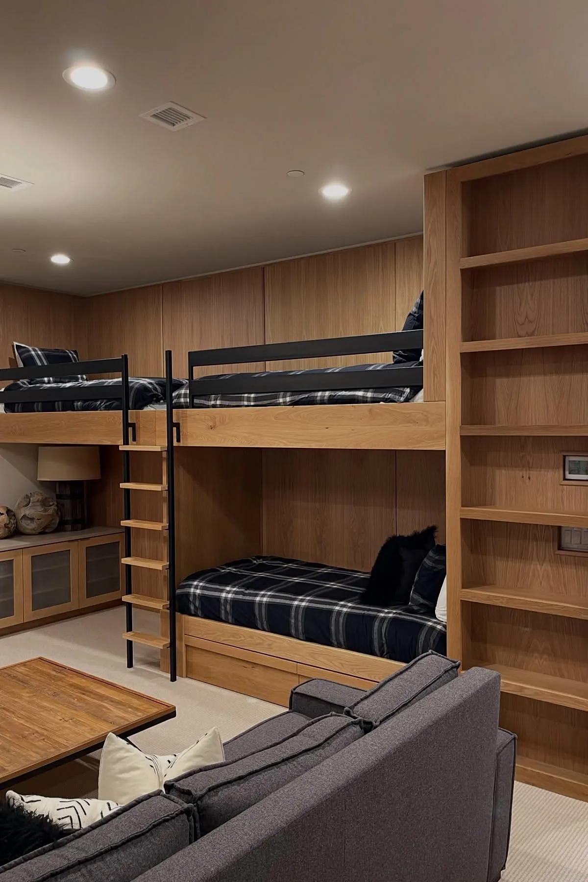 Built-in bunk beds with black railings, plaid bedding, wooden frame, and integrated shelving in a modern room.