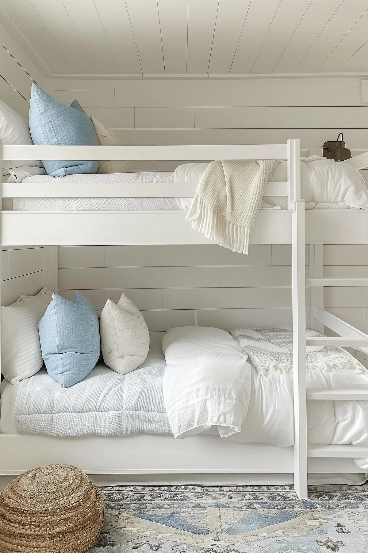White bunk beds with blue pillows and textured rug on floor.