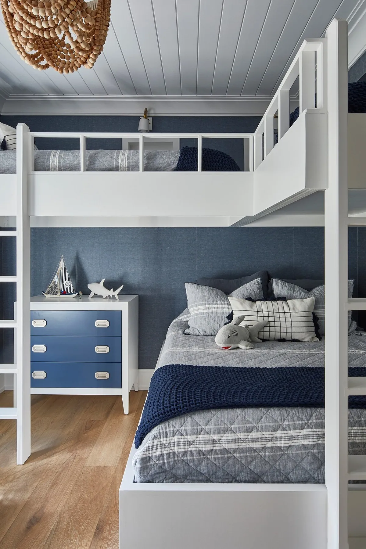 White built-in bunk beds with blue accent walls, nautical decor, plush bedding, and a stylish dresser create a serene atmosphere.