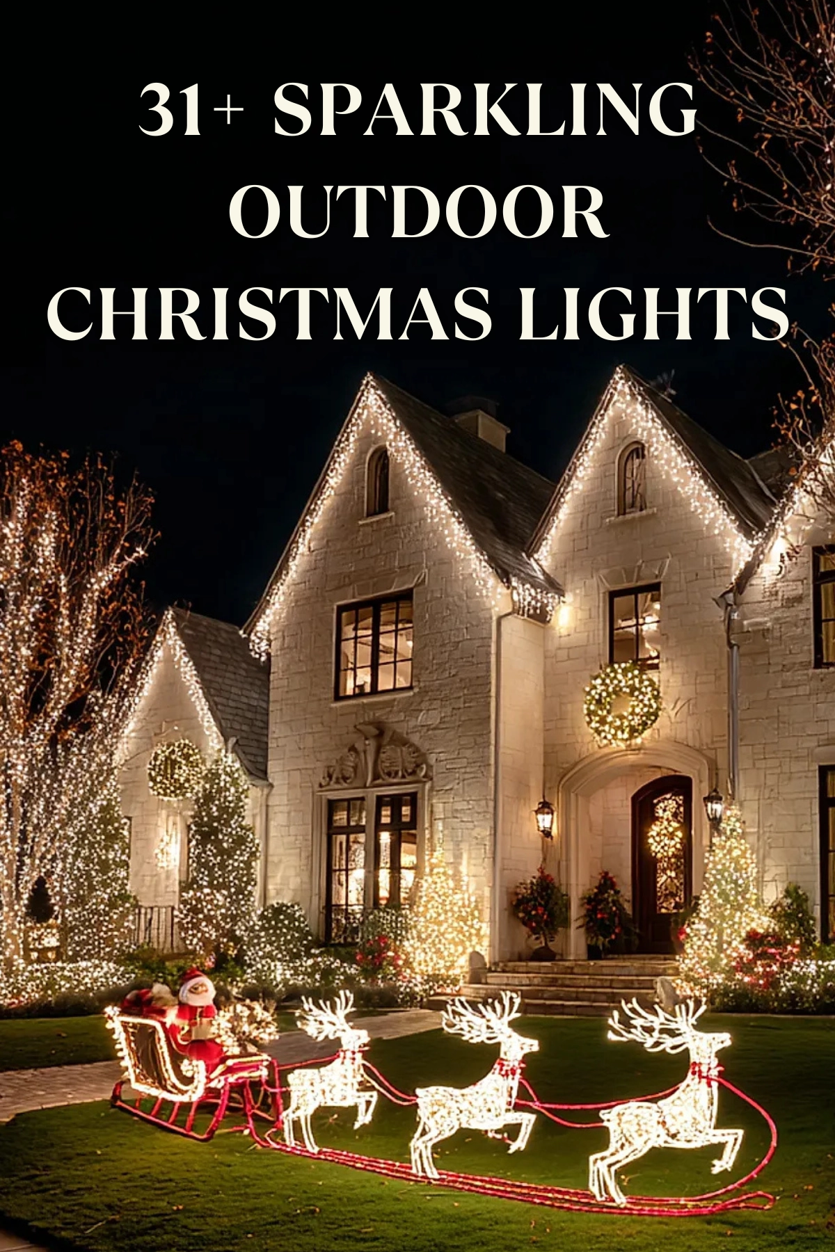 Stone house decorated with warm white outdoor christmas lights outlining the roof peaks and windows, trees wrapped in twinkling white lights, and a glowing light sculpture of Santa in a sleigh pulled by three reindeer on the green lawn at night.
