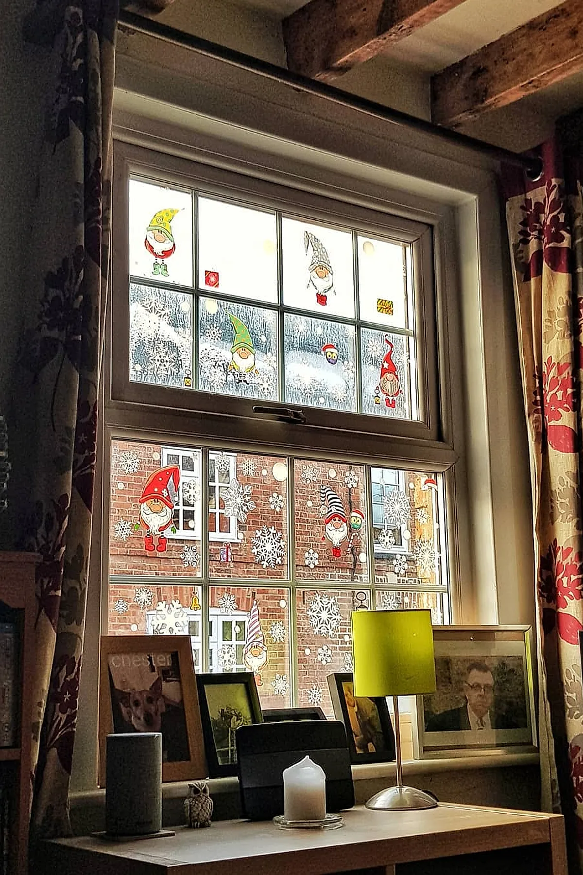 Holiday window art featuring colorful gnome stickers in red, green, and yellow hats alongside scattered white snowflake decals on multiple glass panes for a playful Christmas window idea.