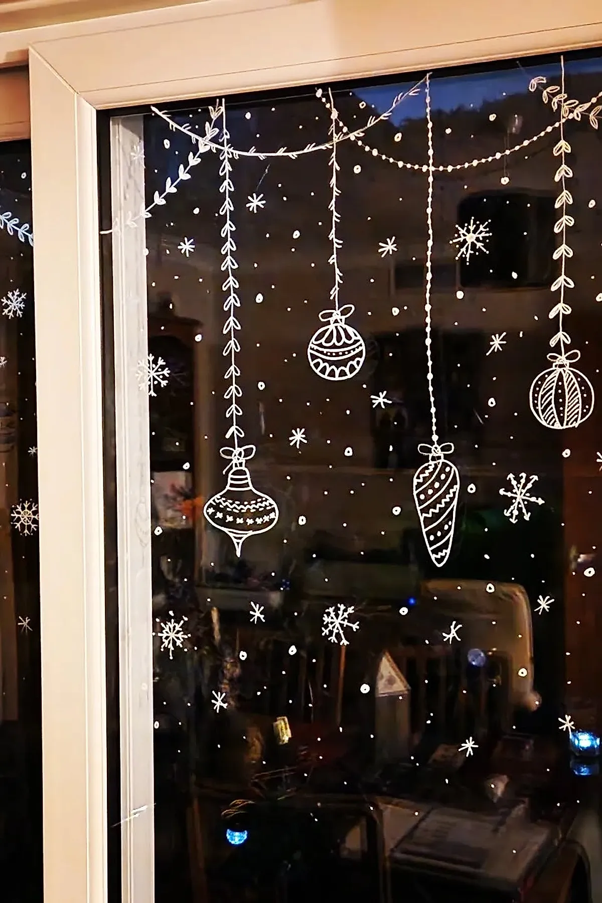 Christmas window painting with white hanging ornaments and garlands surrounded by scattered painted snowflakes and dots, creating an easy and elegant holiday window art idea.