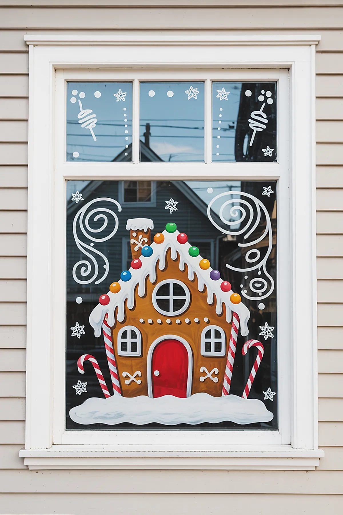 Christmas window art featuring a colorful gingerbread house with a red door, white icing roof, and candy cane details surrounded by snowflakes and swirling icing patterns for a cheerful holiday design.