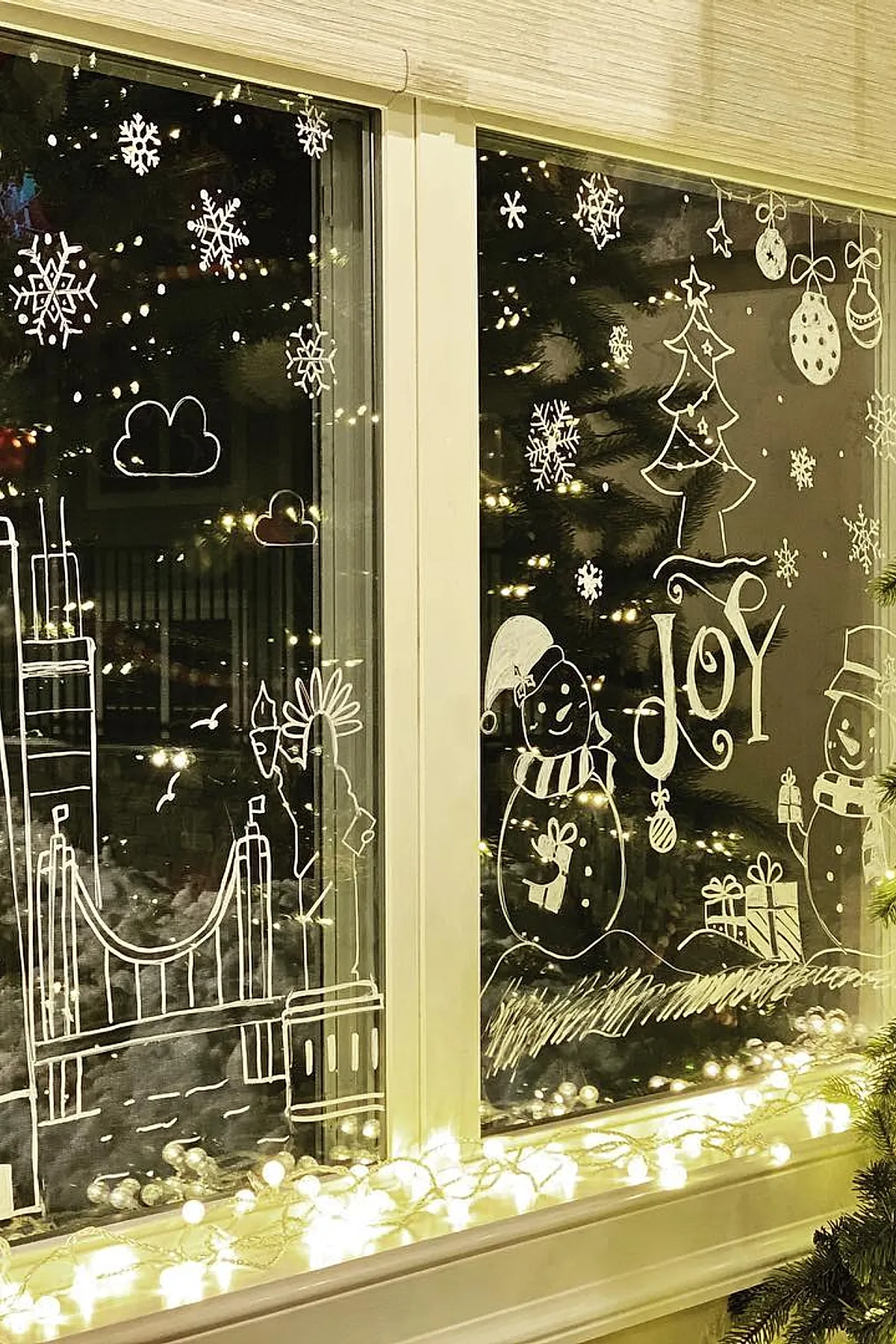Christmas window painting showing smiling snowmen with gifts, a decorated tree, and a white suspension bridge stretching across multiple panes, part of a festive holiday window art display.
