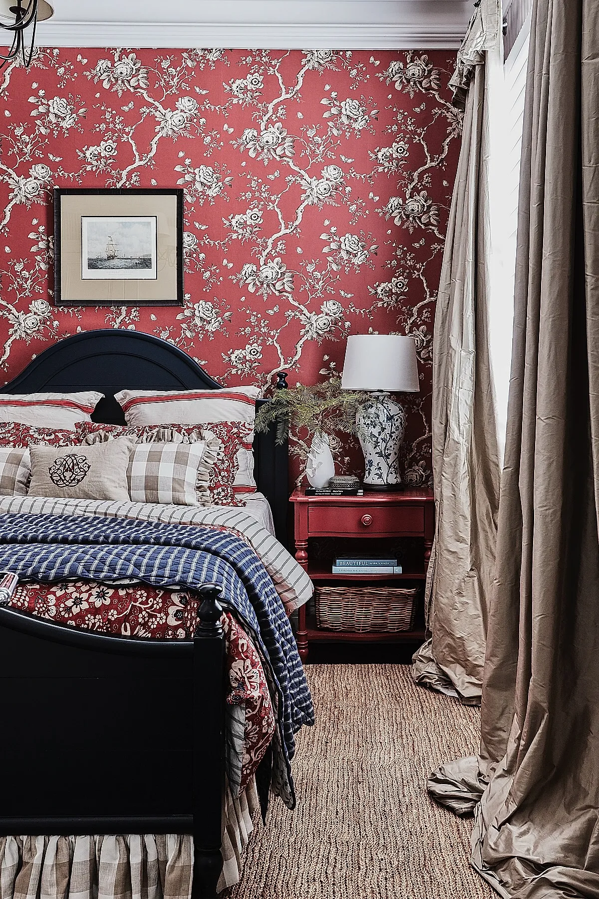 bedroom featuring red floral wallpaper, black wooden bed frame, mixed patterned bedding including stripes and checks, beige curtains, woven floor rug