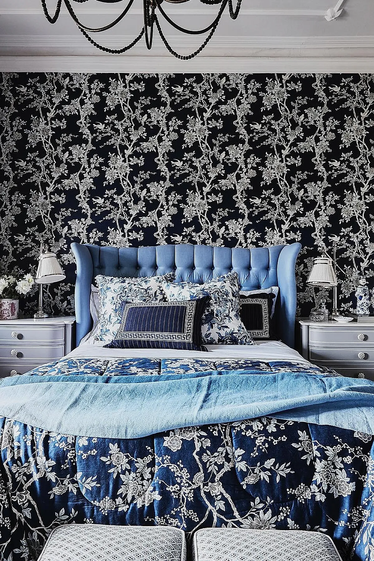bedroom featuring tufted blue wingback headboard, navy wallpaper with white floral pattern, blue and white floral bedding layered with solid light blue throw blanket, white bedside tables with matching lamps