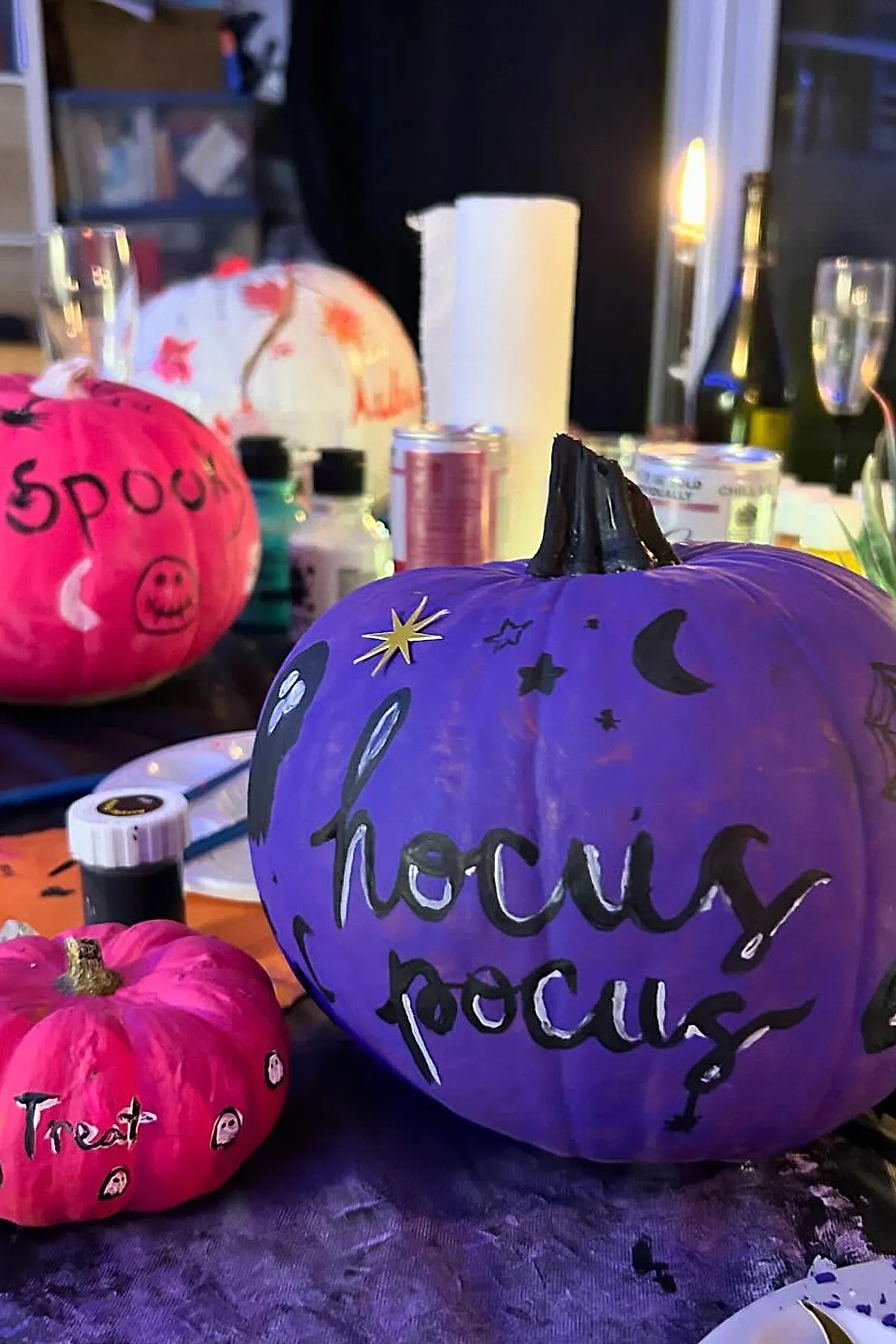 purple pumpkin painted with black lettering saying hocus pocus along with stars moon and ghost shapes next to bright pink pumpkins decorated with spooky faces and treat text on dark table