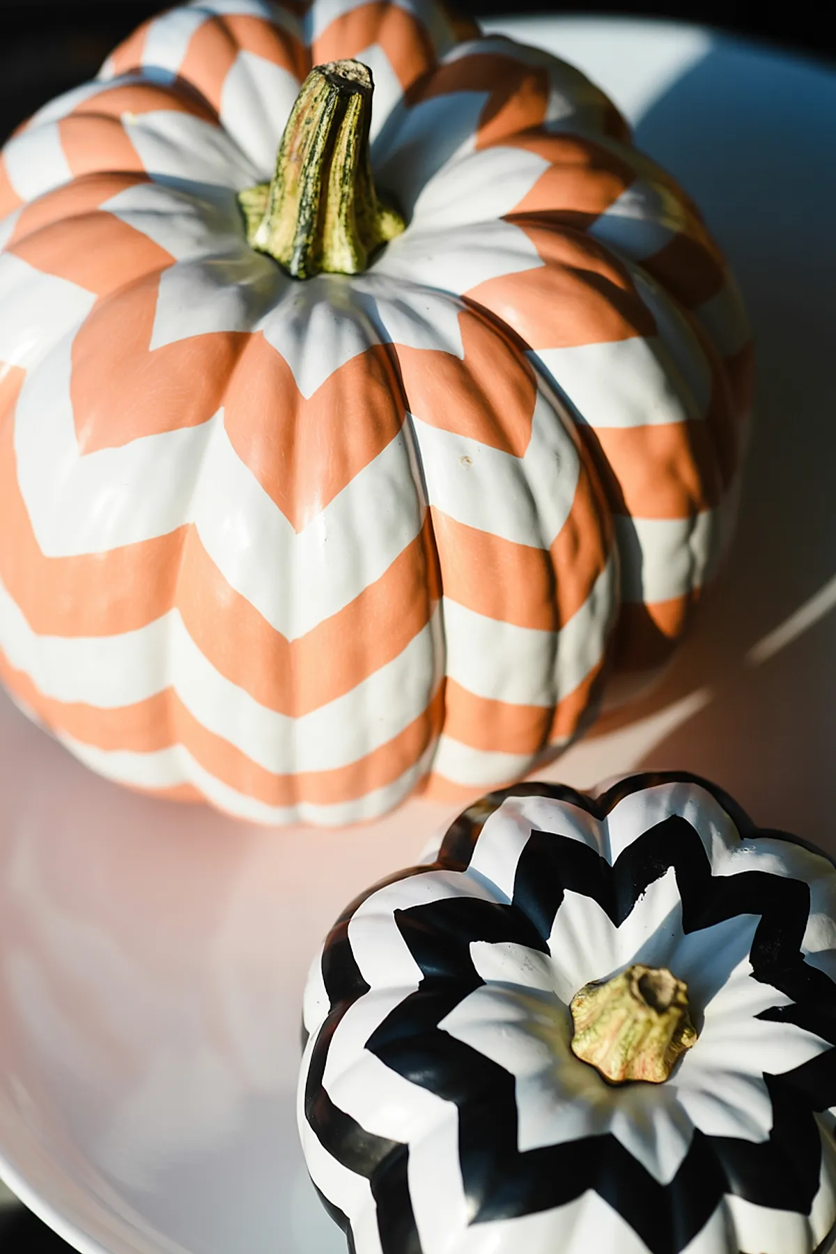 two pumpkins painted with bold chevron patterns one in peach and white, the other in black and white, showing natural stem tops